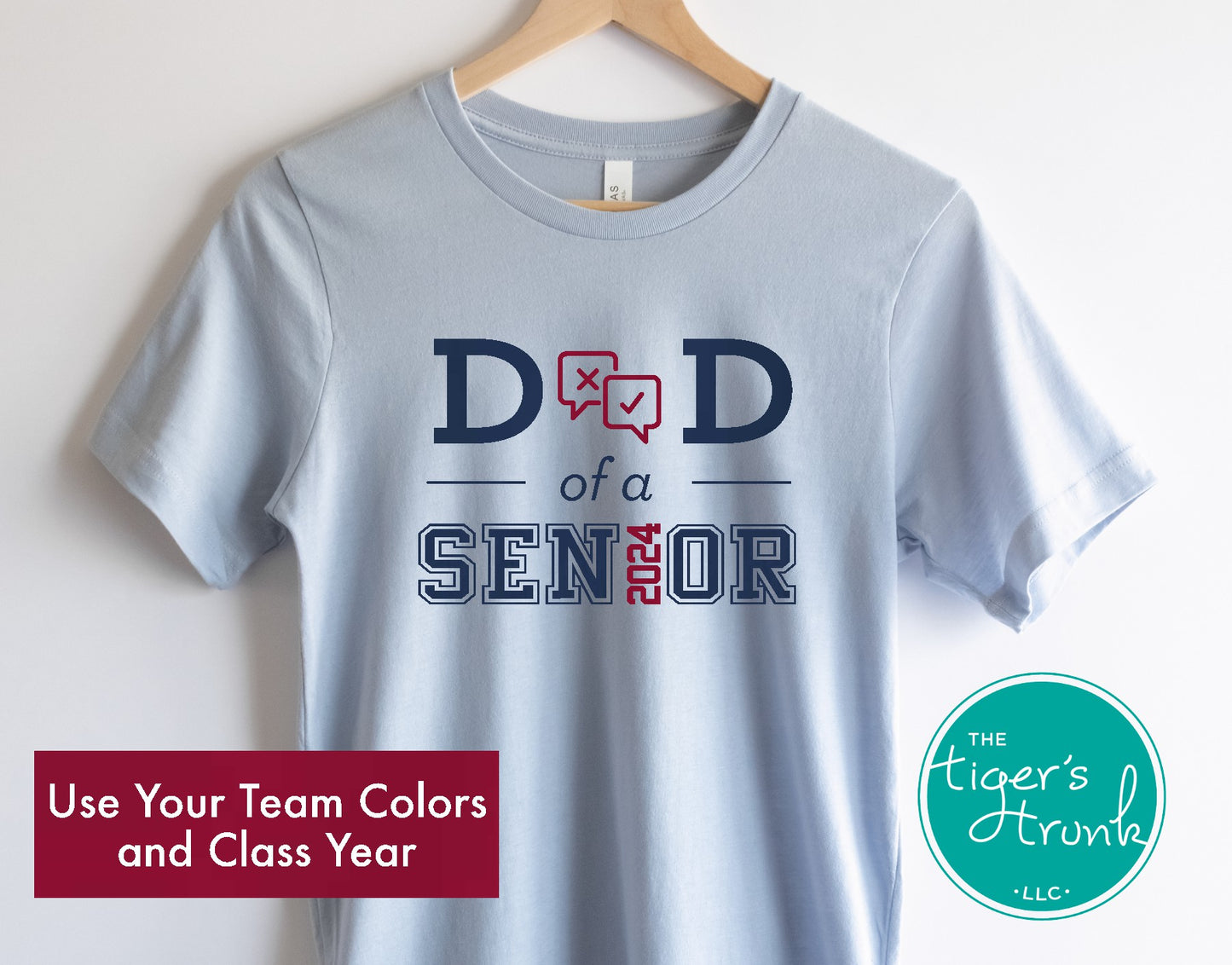 A blue short-sleeved t-shirt with 'DAD OF A SENIOR 2021' printed on the front, along with the letters 'LHS' and a graduation cap icon, hanging on a wooden hanger.