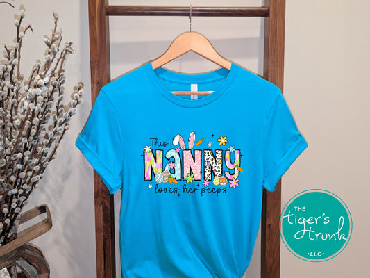 Easter t-shirt with "Nanny" in spring print font decorated with bunnies, eggs, and flowers, perfect for holiday wear and springtime fun