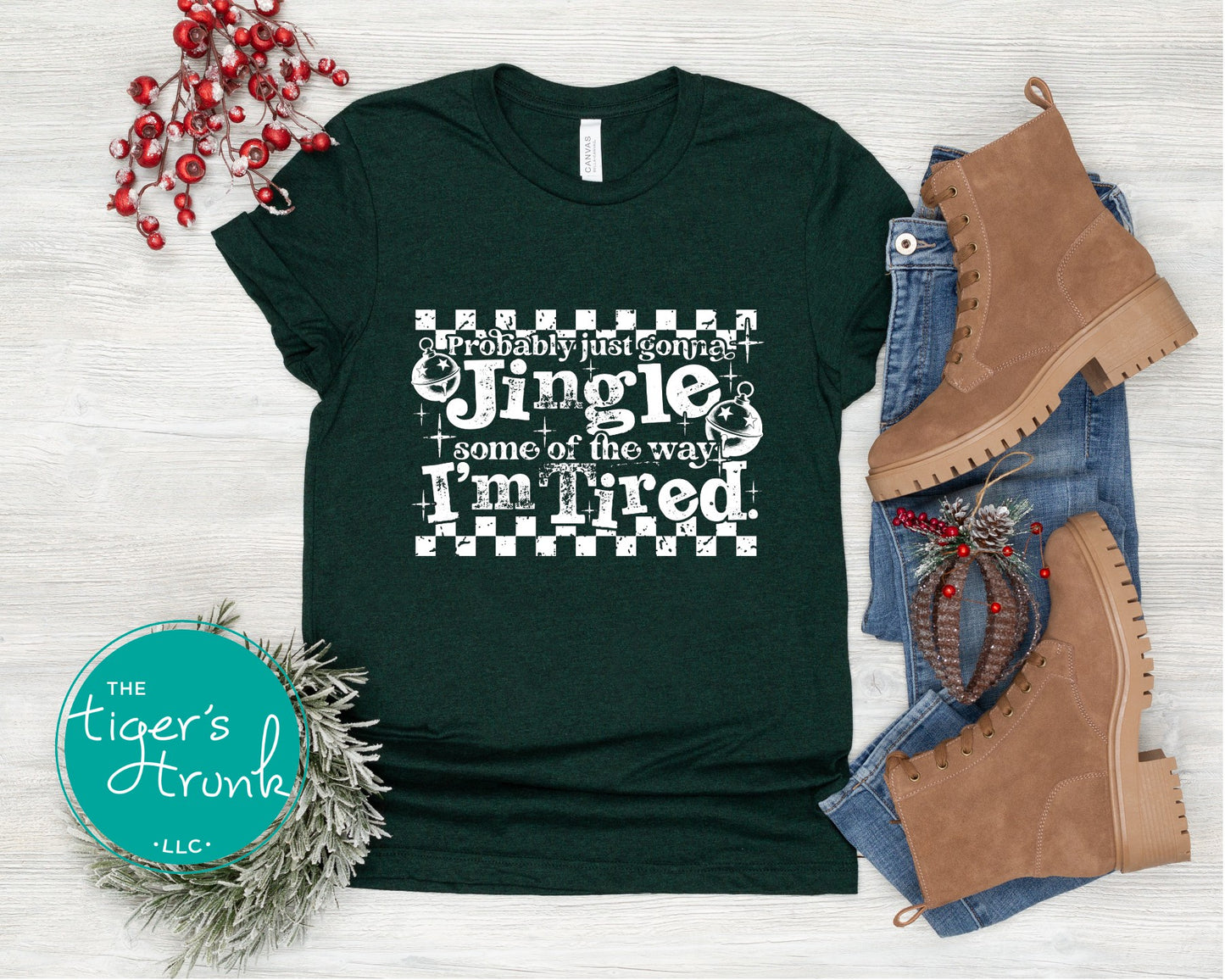 Green t-shirt with Christmas-themed text, boots, and decorations on a light wooden surface.