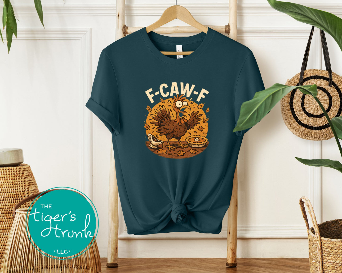 Blue t-shirt with a cartoon character and text 'F-CAW-F' on a hanger against a white wall.