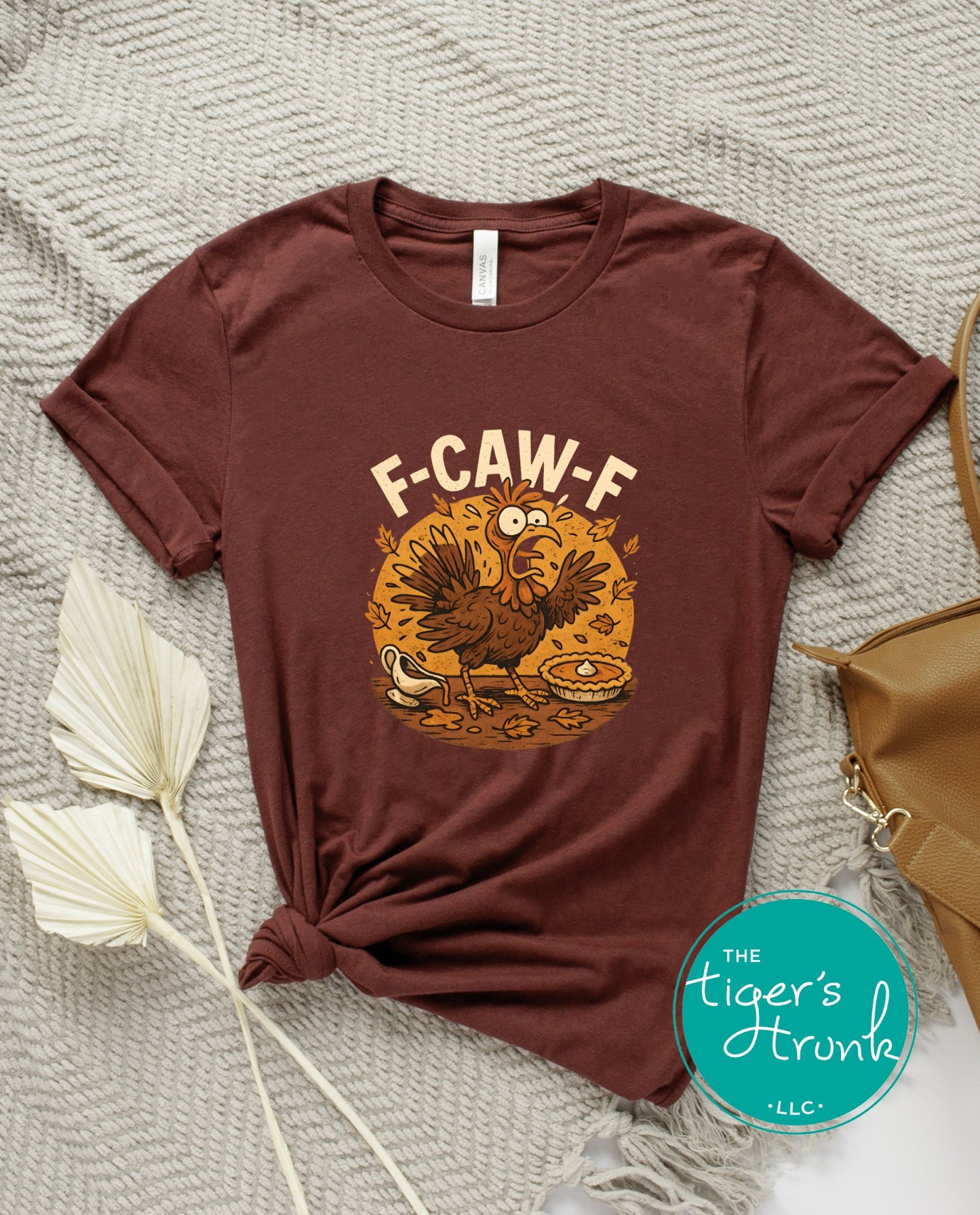 Brown t-shirt with a graphic design and text on a textured surface, featuring the brand 'The Tiger's Trunk'.