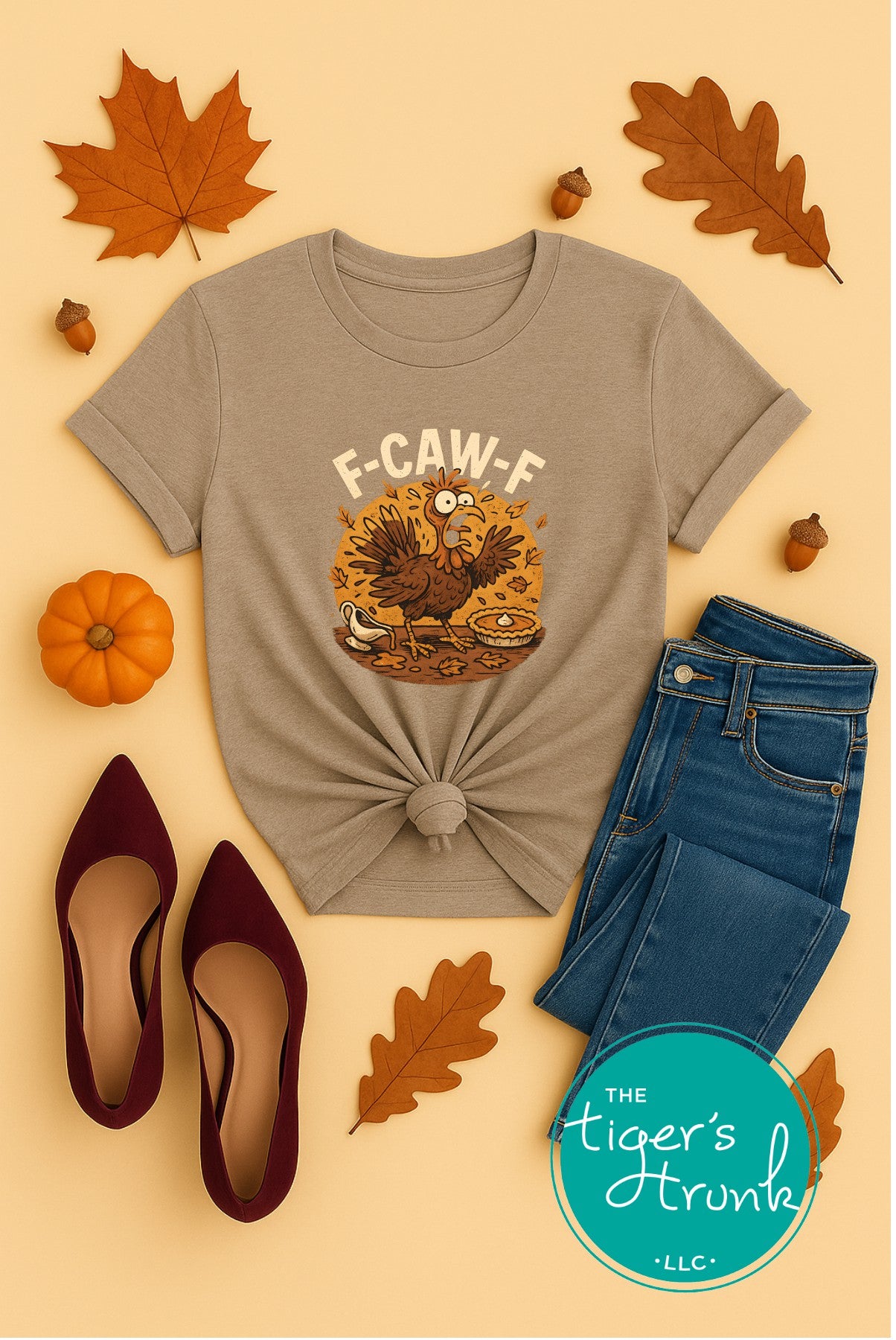 Gray t-shirt with a turkey graphic and text, paired with jeans and shoes on a beige background with fall leaves and pumpkins.