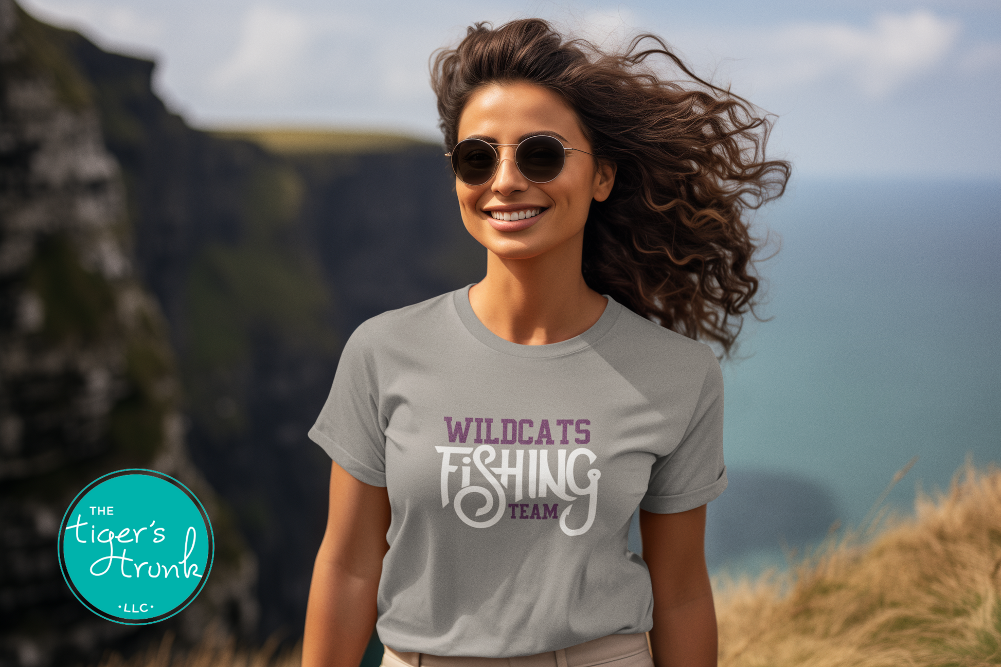 woman wearing gray fishing team shirt personalized with Wildcats mascot in purple and white standing near ocean cliffs