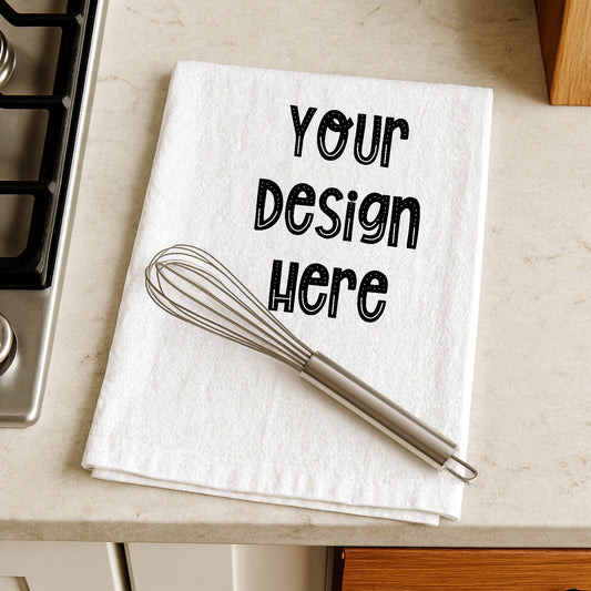 White towel with 'Your Design Here' text and a whisk on a kitchen counter.