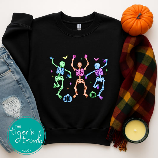 Black sweatshirt with colorful skeleton design, surrounded by denim jeans, a plaid scarf, and a small pumpkin on a white background.