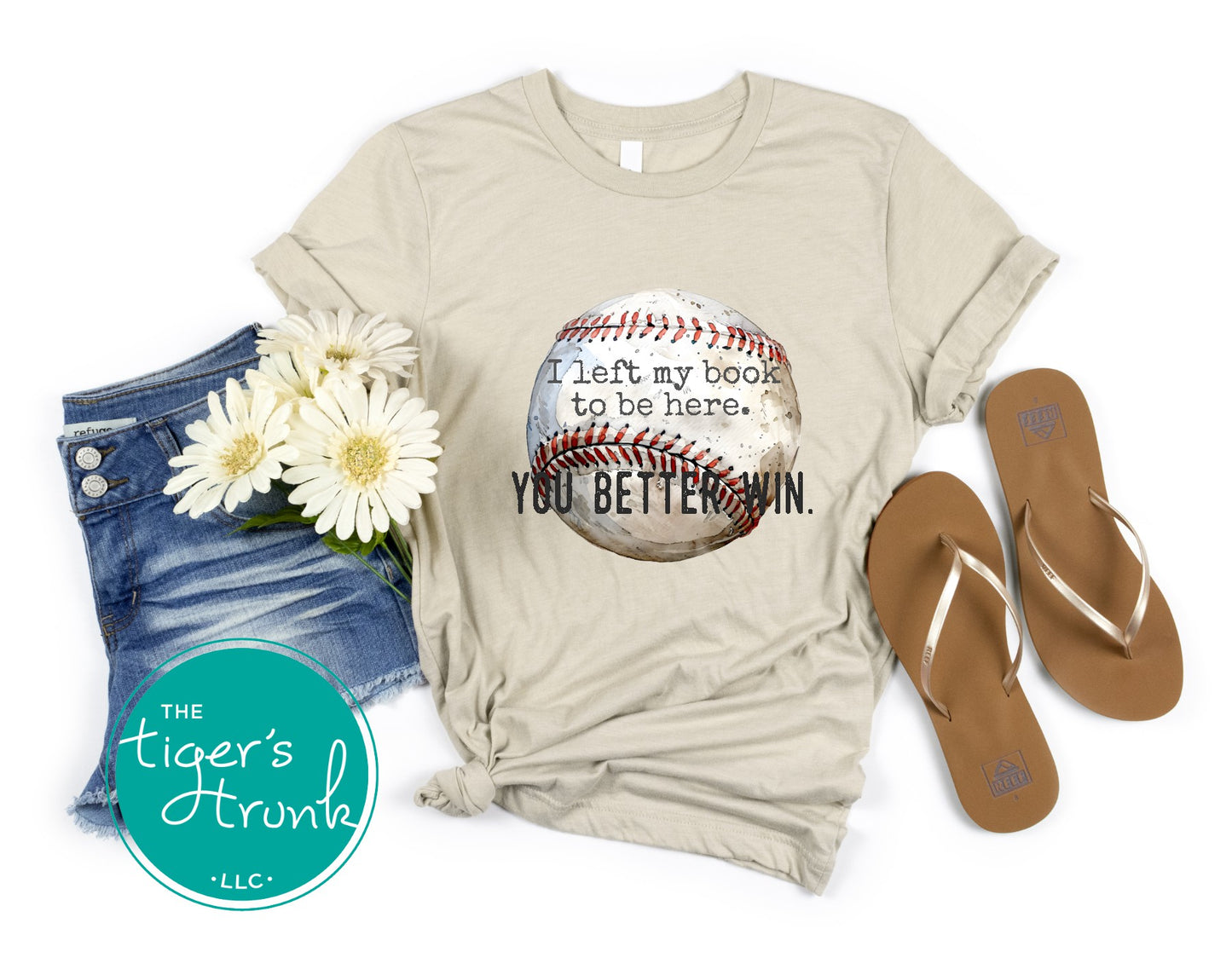 Beige t-shirt with baseball graphic and text, denim shorts, sandals, and flowers on a white background.