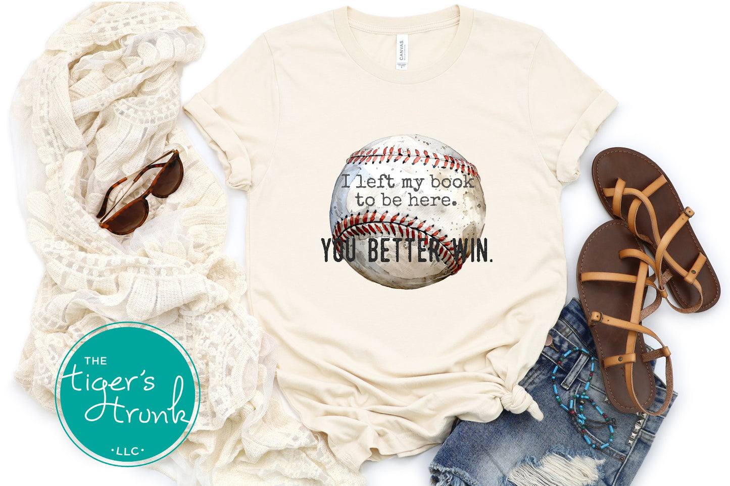 Beige t-shirt with baseball graphic and text, scarf, sunglasses, and sandals on a white background.