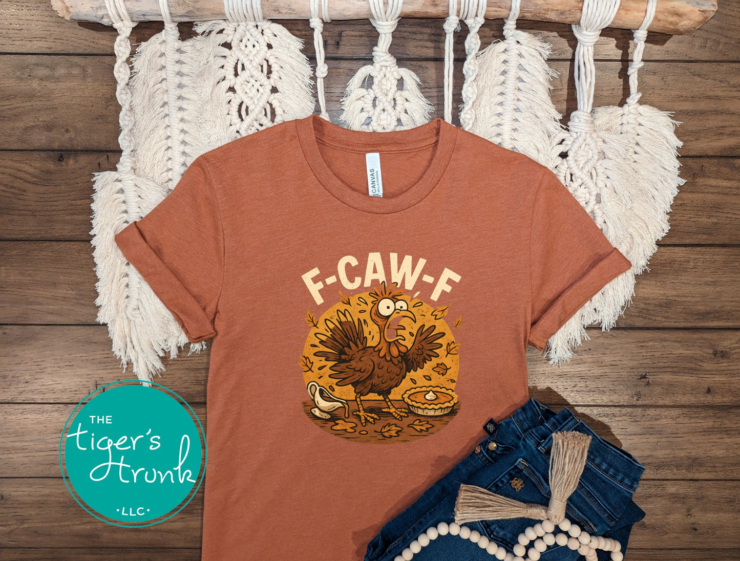 Brown t-shirt with a graphic design on a wooden surface with macrame hanging.