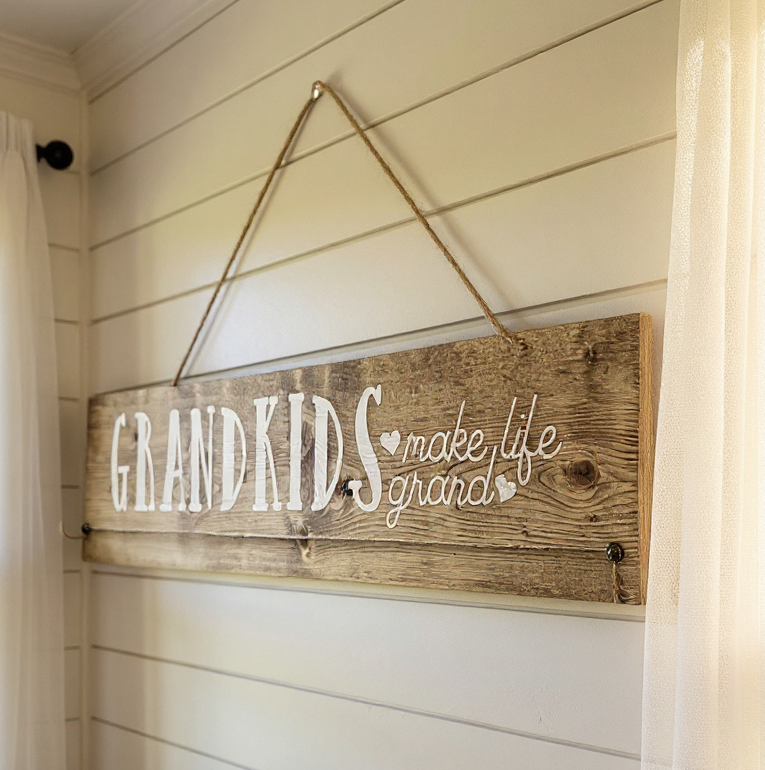 Wooden sign with 'GRAND KIDS make life grand' text hanging on a wall.