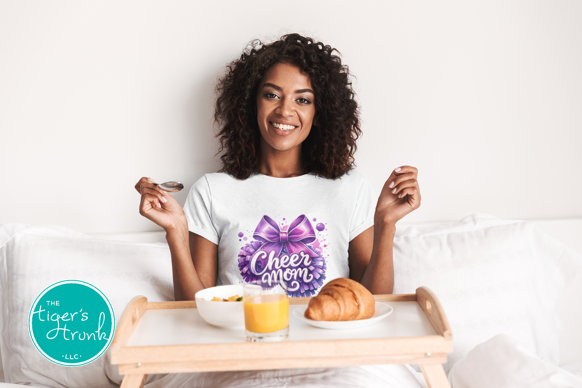 Woman in a white t-shirt with a purple bow design, sitting in bed with a tray of food.