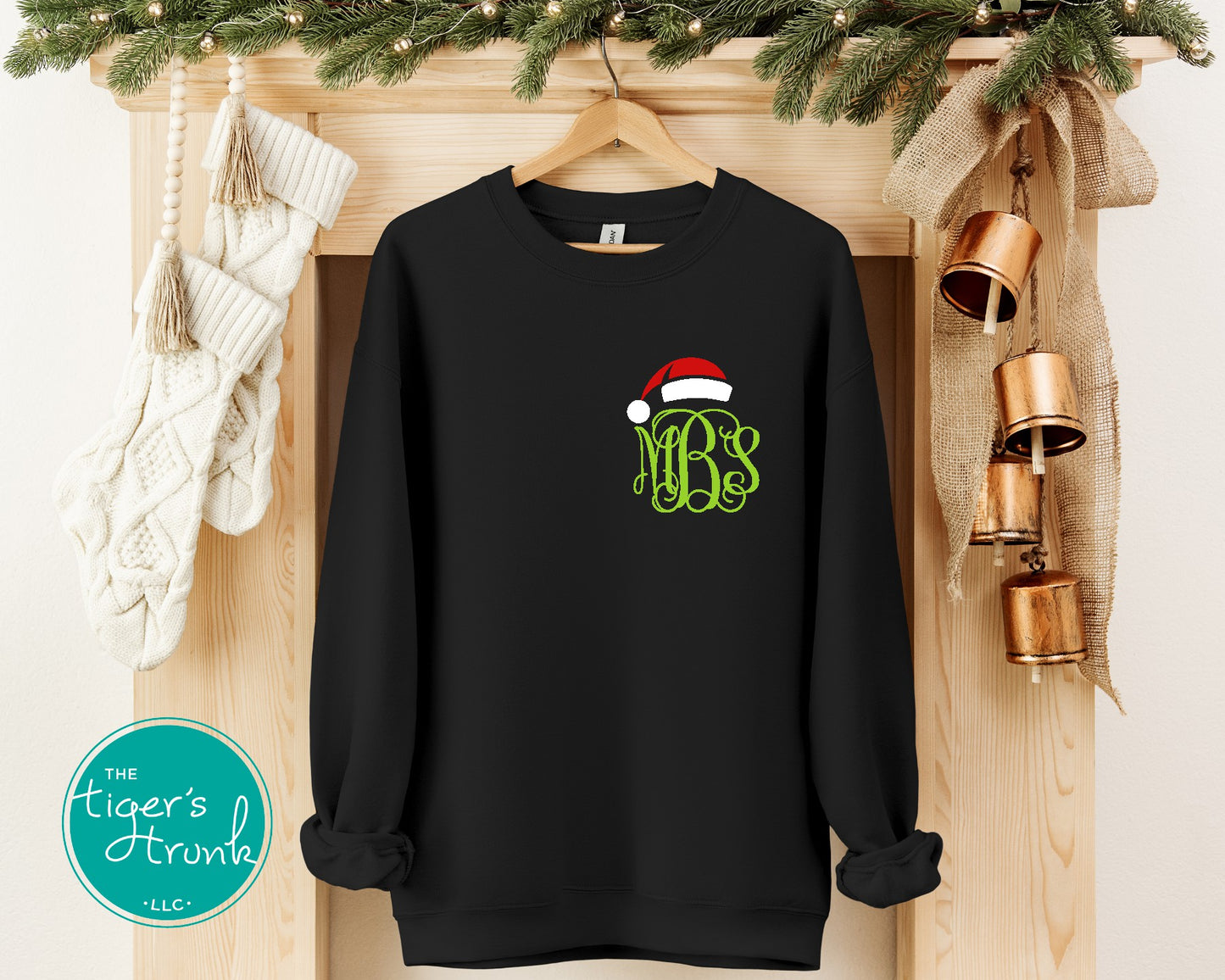 Black sweatshirt with a Santa hat and monogram on a wooden surface with Christmas decorations.