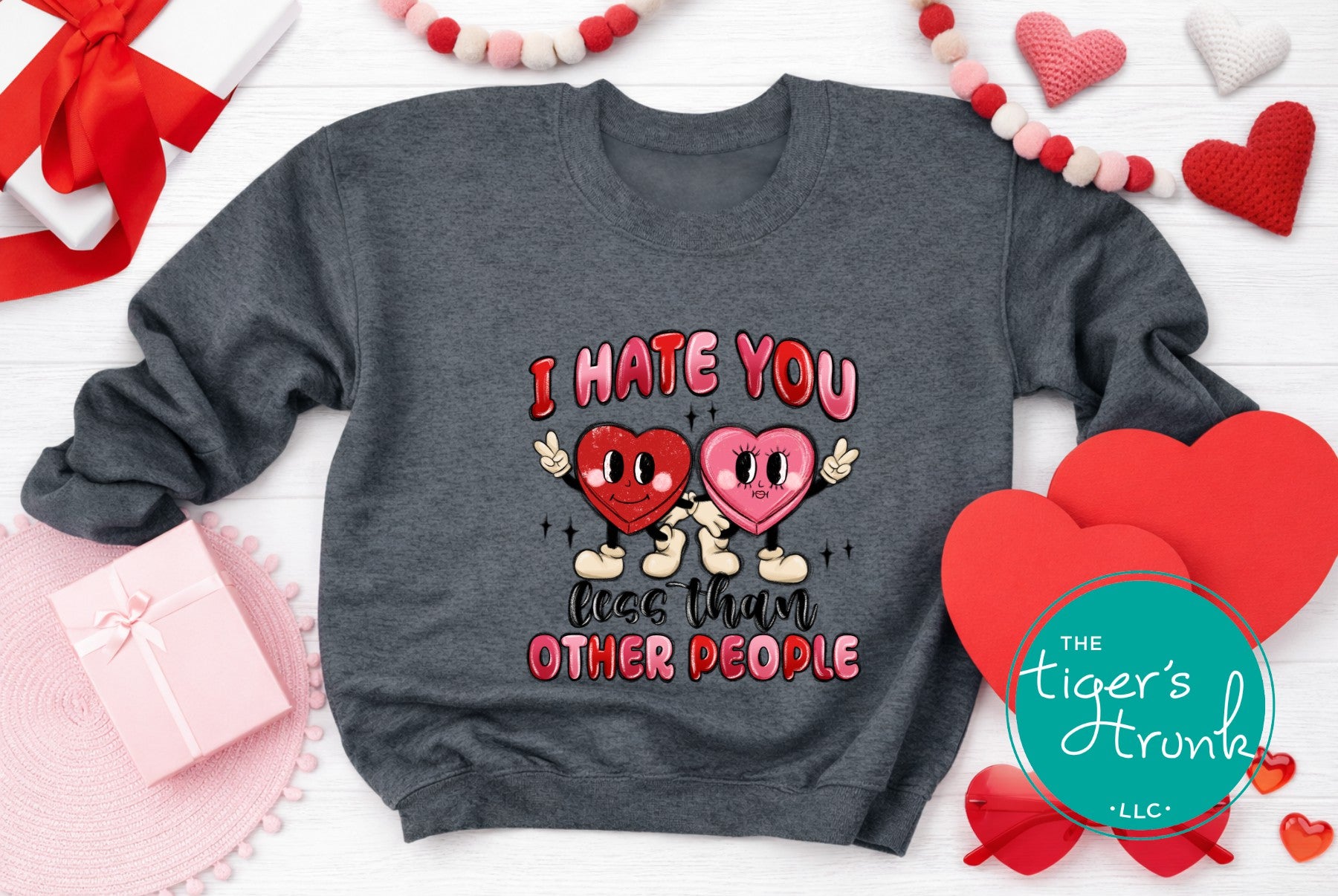 Gray sweatshirt with cartoon hearts and text, surrounded by heart-shaped decorations and a gift box.