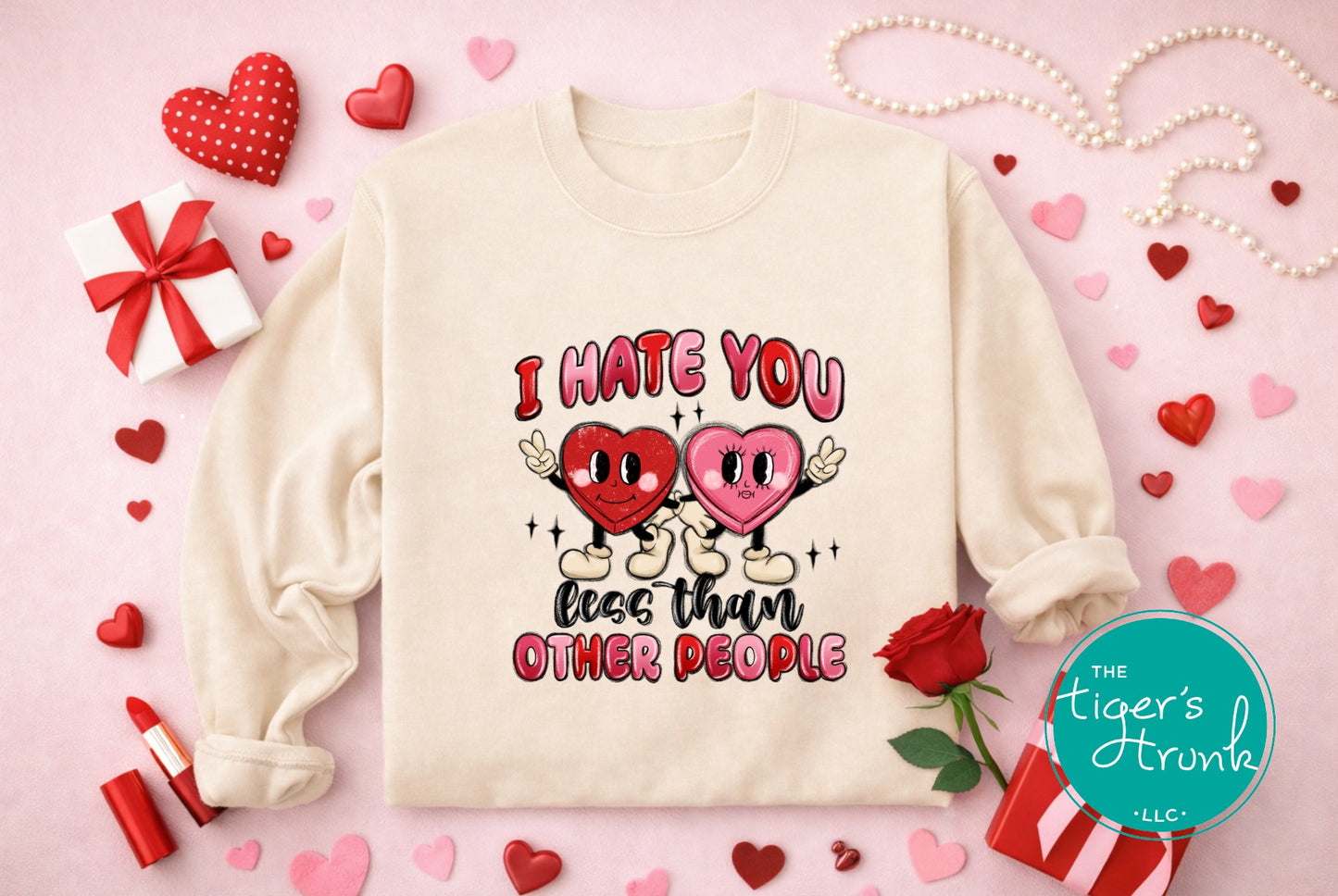 White sweatshirt with 'I Hate You Less Than Other People' text and hearts on a pink background with hearts and a gift box.