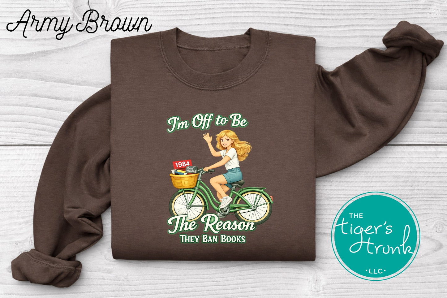 Army brown progressive sweatshirt featuring a reader riding a bicycle with banned books and the phrase I’m off to be the reason they ban books