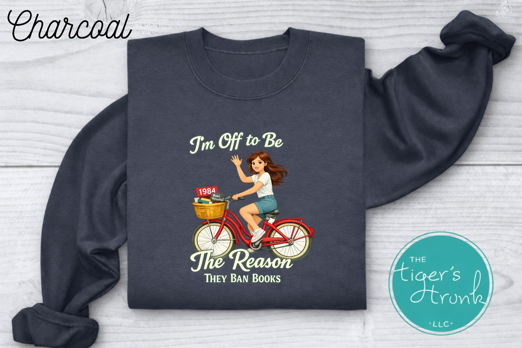 Charcoal gray progressive sweatshirt featuring a reader riding a bicycle with banned books and the phrase I’m off to be the reason they ban books