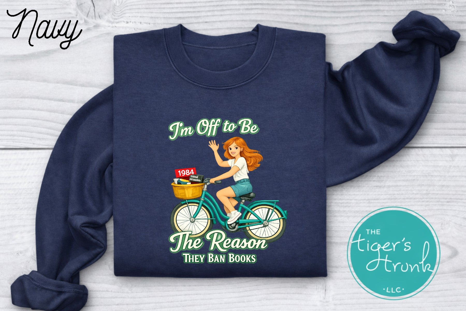 Navy blue progressive sweatshirt featuring a reader riding a bicycle with banned books and the phrase I’m off to be the reason they ban books