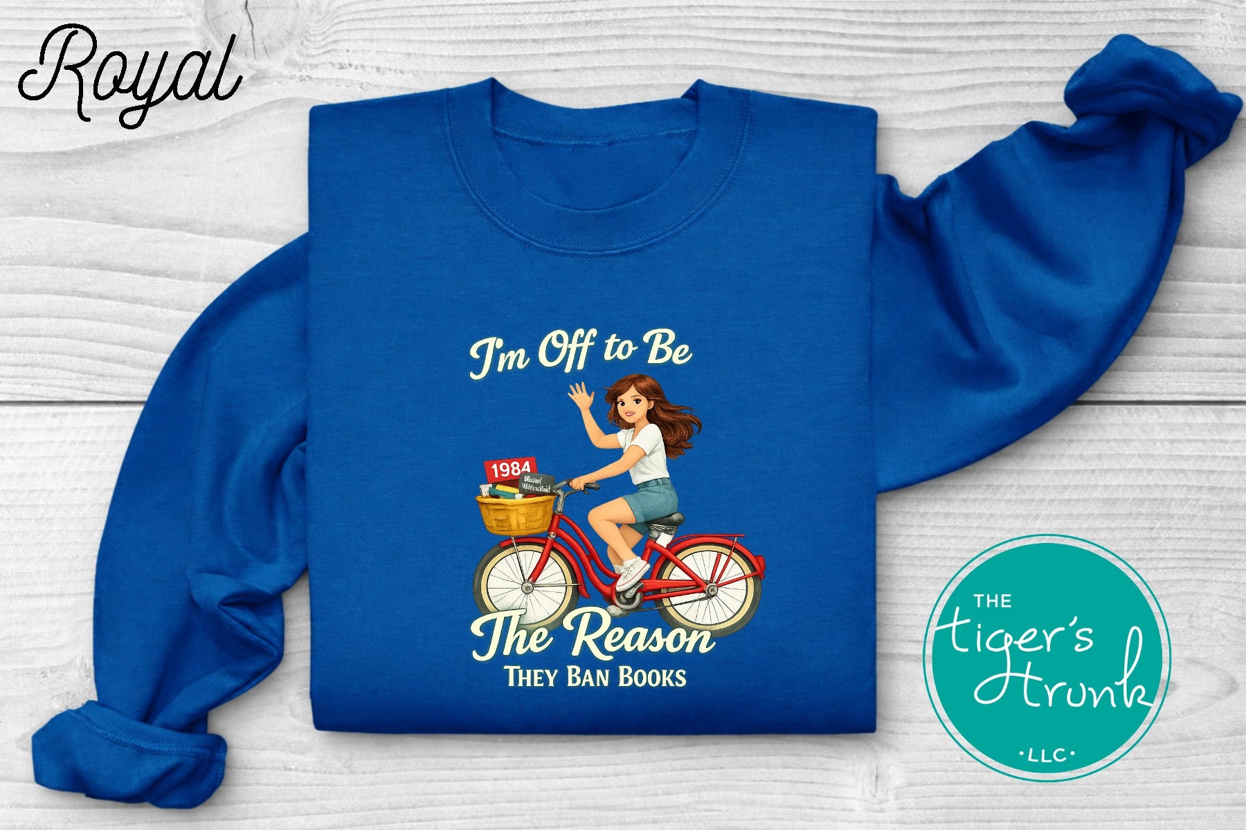 Royal blue progressive sweatshirt featuring a reader riding a bicycle with banned books and the phrase I’m off to be the reason they ban books