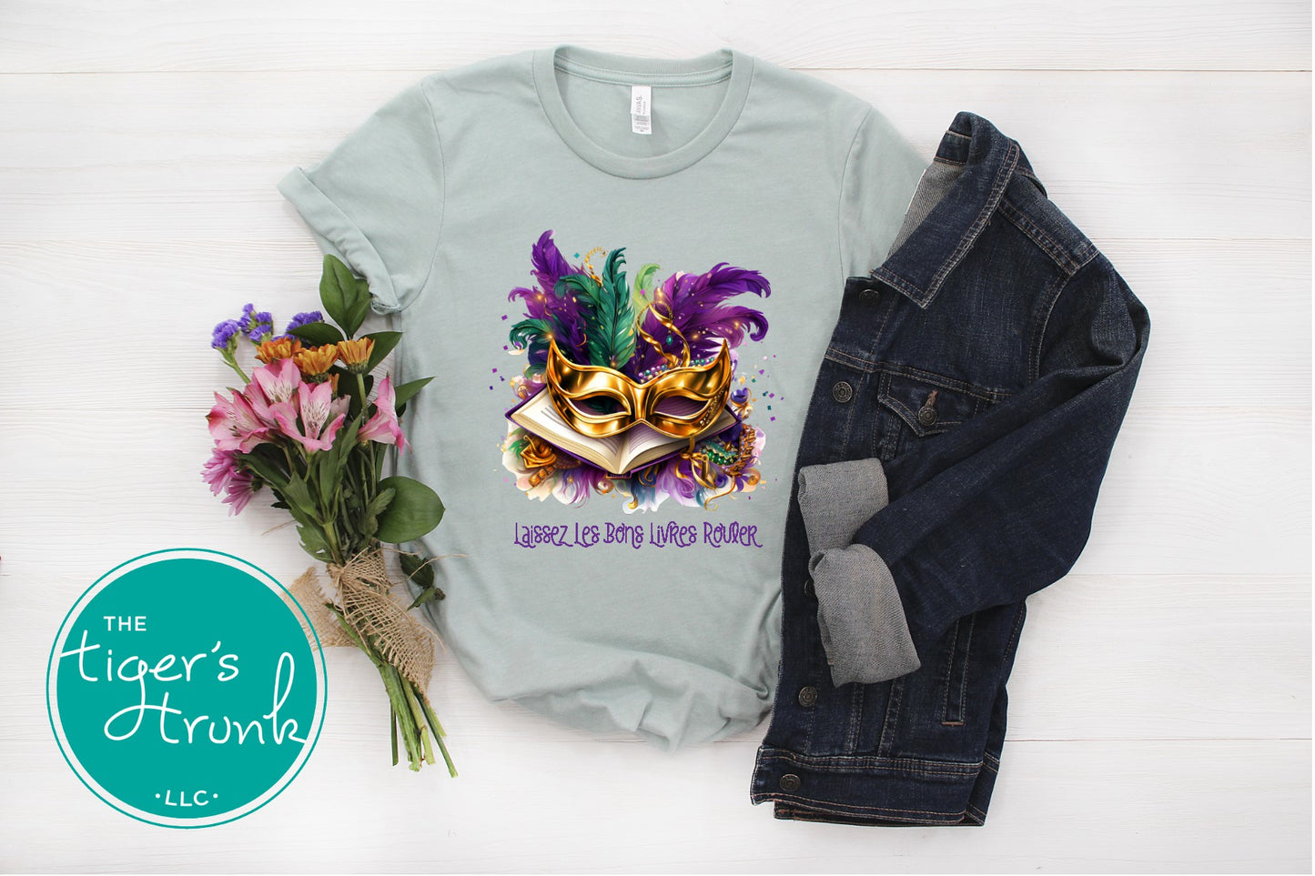 Mardi Gras shirt with books, masks, feathers, and beads, featuring the phrase "Laissez Les Bons Livres Rouler."