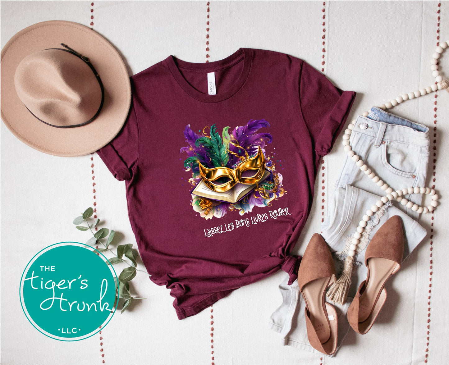 Mardi Gras shirt with books, masks, feathers, and beads, featuring the phrase "Laissez Les Bons Livres Rouler."