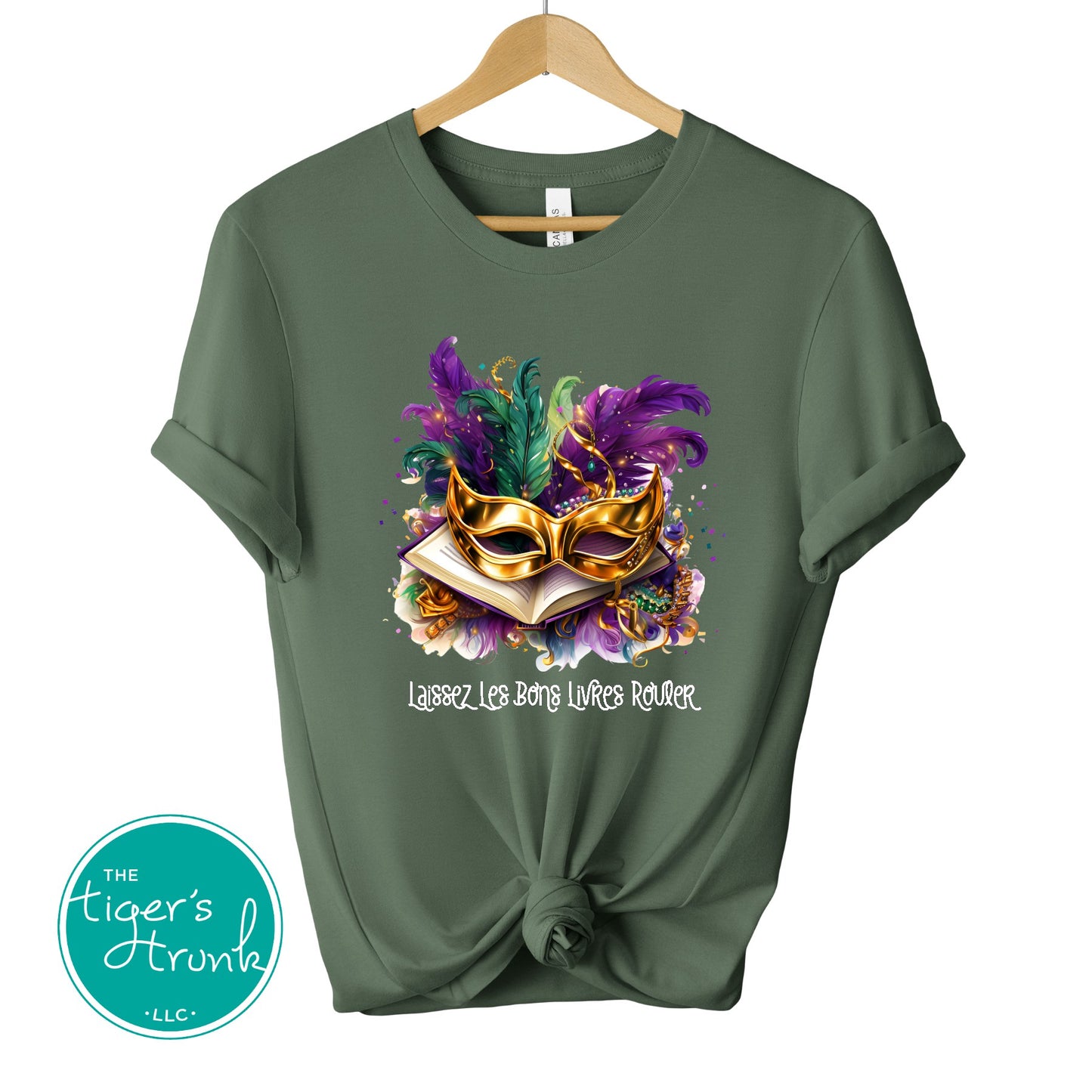 Mardi Gras shirt with books, masks, feathers, and beads, featuring the phrase "Laissez Les Bons Livres Rouler."