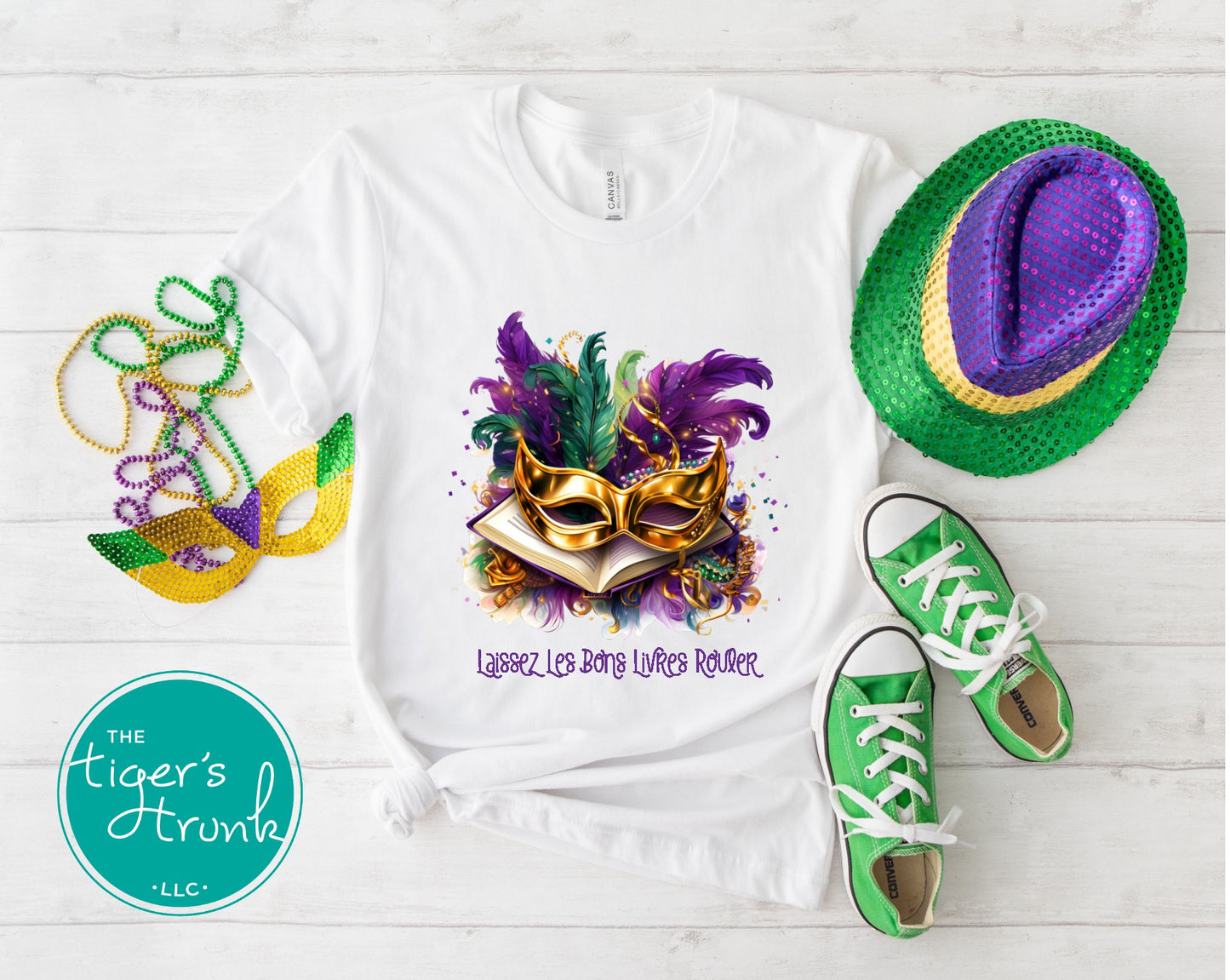 Mardi Gras shirt with books, masks, feathers, and beads, featuring the phrase "Laissez Les Bons Livres Rouler."