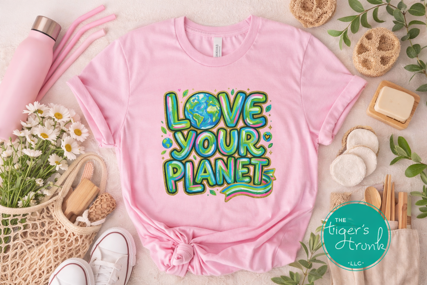 Pink t-shirt with 'Love Your Planet' text on a light surface with lifestyle items.