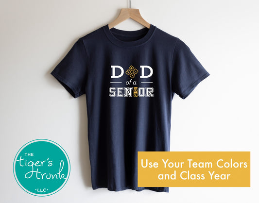A navy blue short-sleeve t-shirt with the text 'DAD OF A SENIOR' and the graduation year '2025' printed on the front. The shirt is displayed on a wooden hanger with a logo and text 'The Tiger's Trunk, LLC' at the bottom.