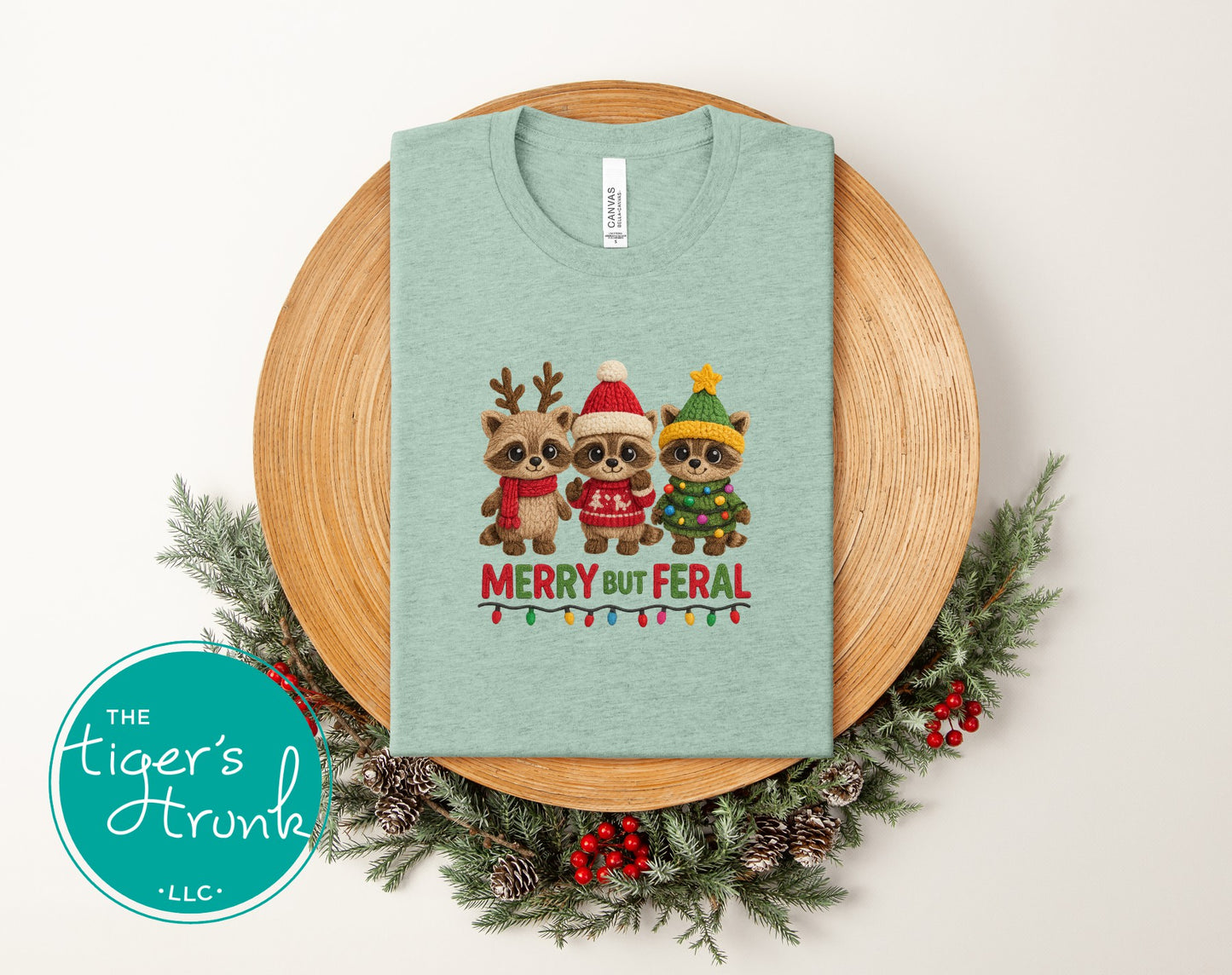 Green t-shirt with Christmas-themed design of three raccoons on a wooden plate with festive decorations.