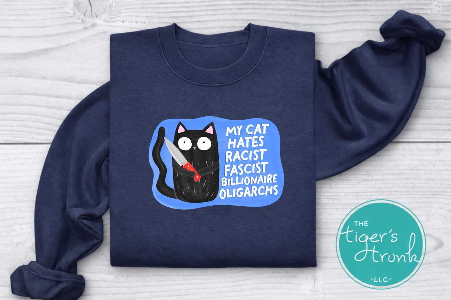 Navy blue sweatshirt with a graphic of a cat and text on a light wooden surface, featuring 'The Tiger's Trunk' logo.