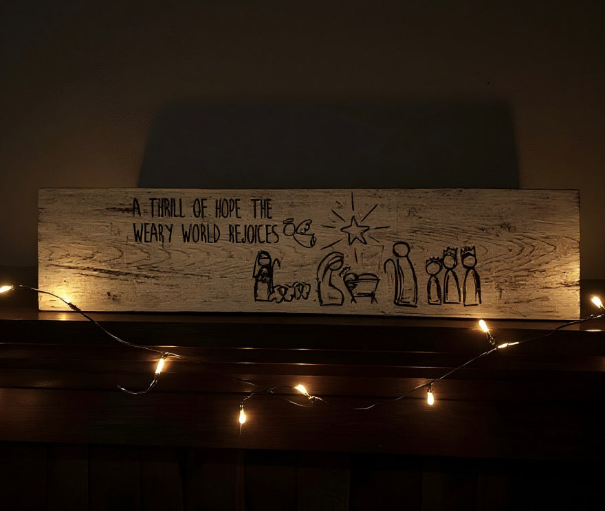 hand-painted nativity wood sign on a mantel with soft Christmas lights