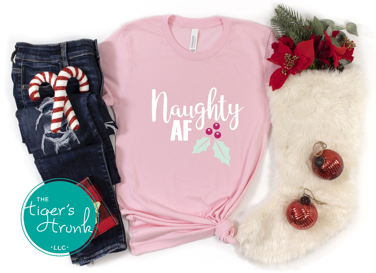Pink t-shirt with 'Naughty AF' text, jeans, and Christmas decorations on a white background.