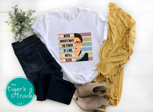 White t-shirt with graphic design and text, paired with jeans and a yellow sweater on a white surface.
