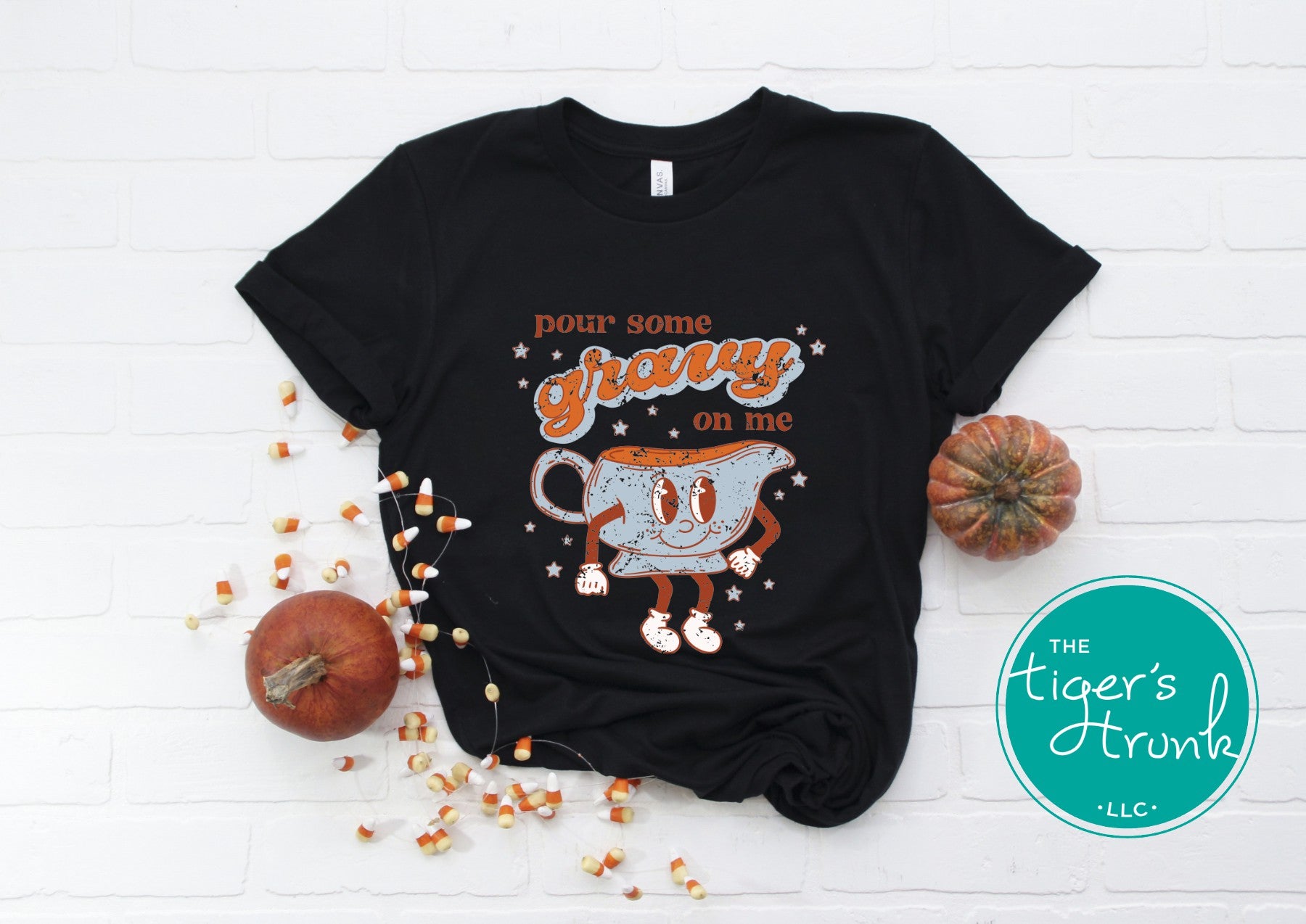Black t-shirt with a graphic design of a candy corn and text, surrounded by pumpkins and corn on a white background.