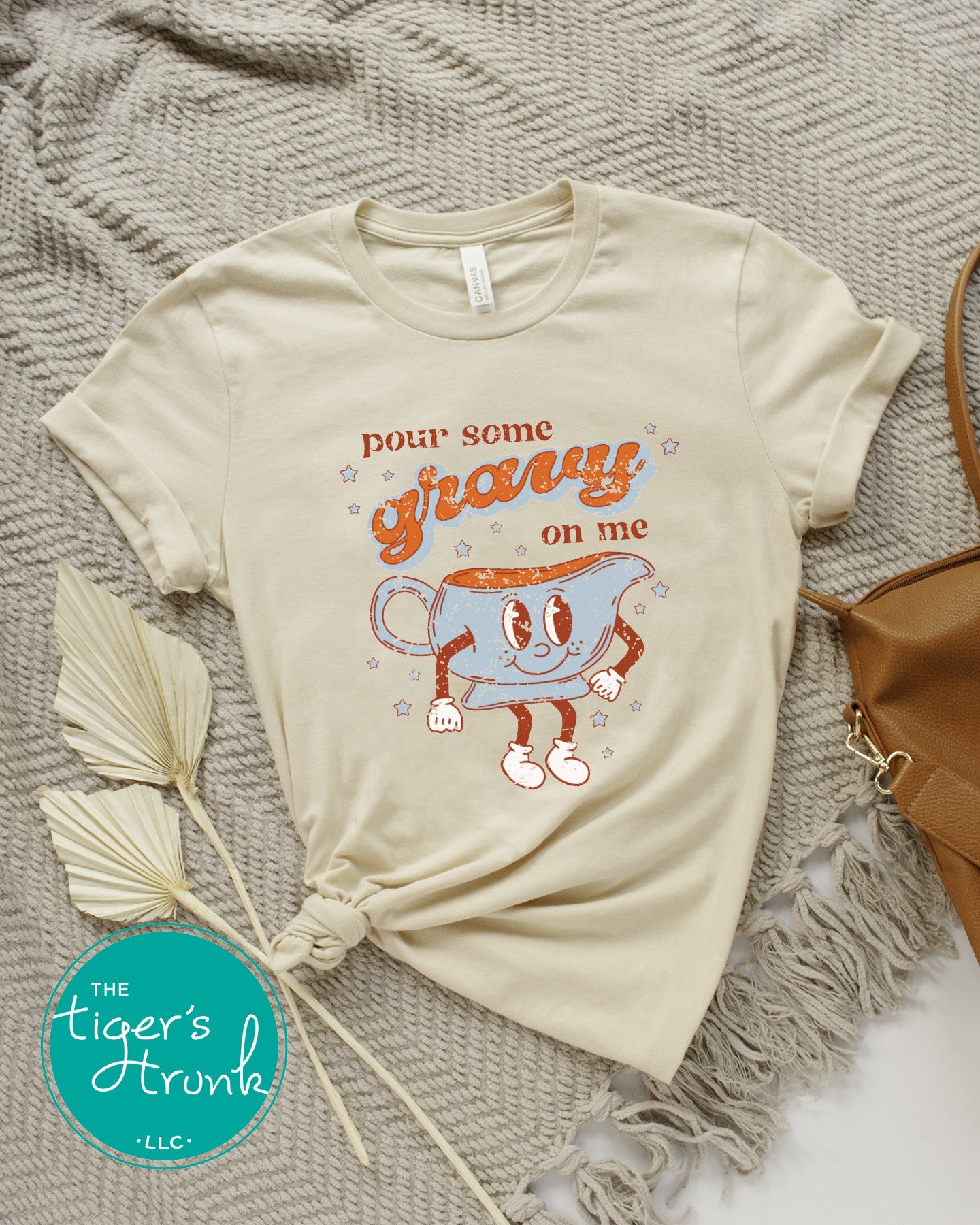 Beige t-shirt with cartoon gravy boat graphic and text 'Pour some gravy on me' on a textured surface.