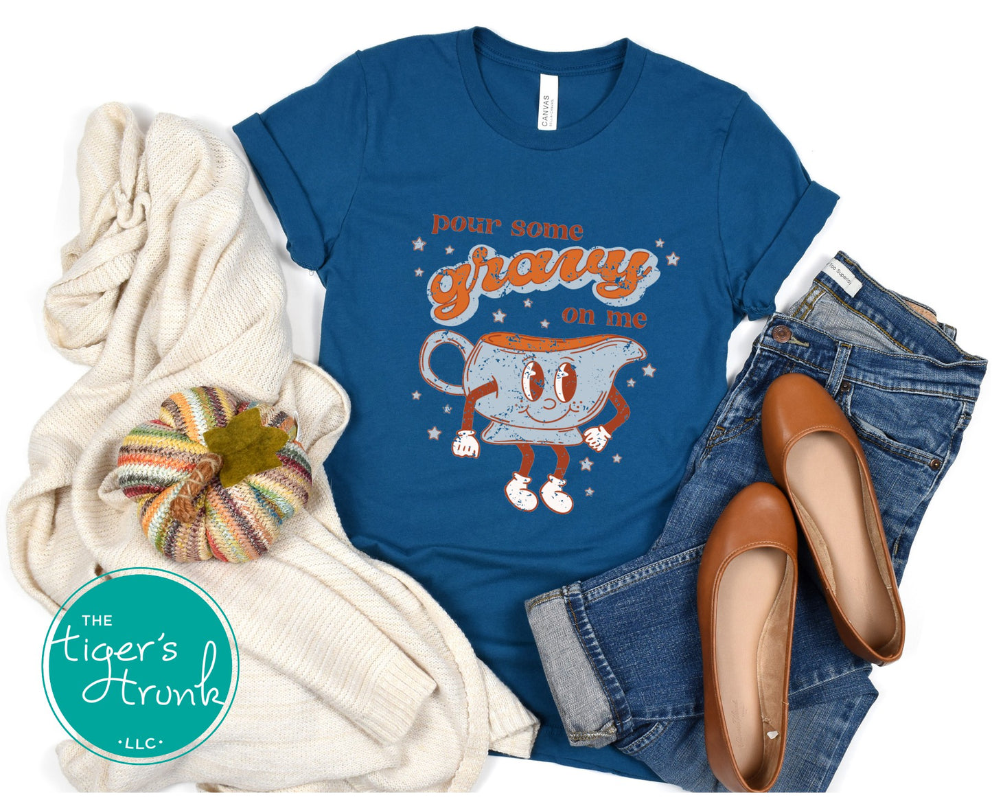 Blue t-shirt with cartoon gravy boat graphic and text, surrounded by jeans, shoes, and a blanket.