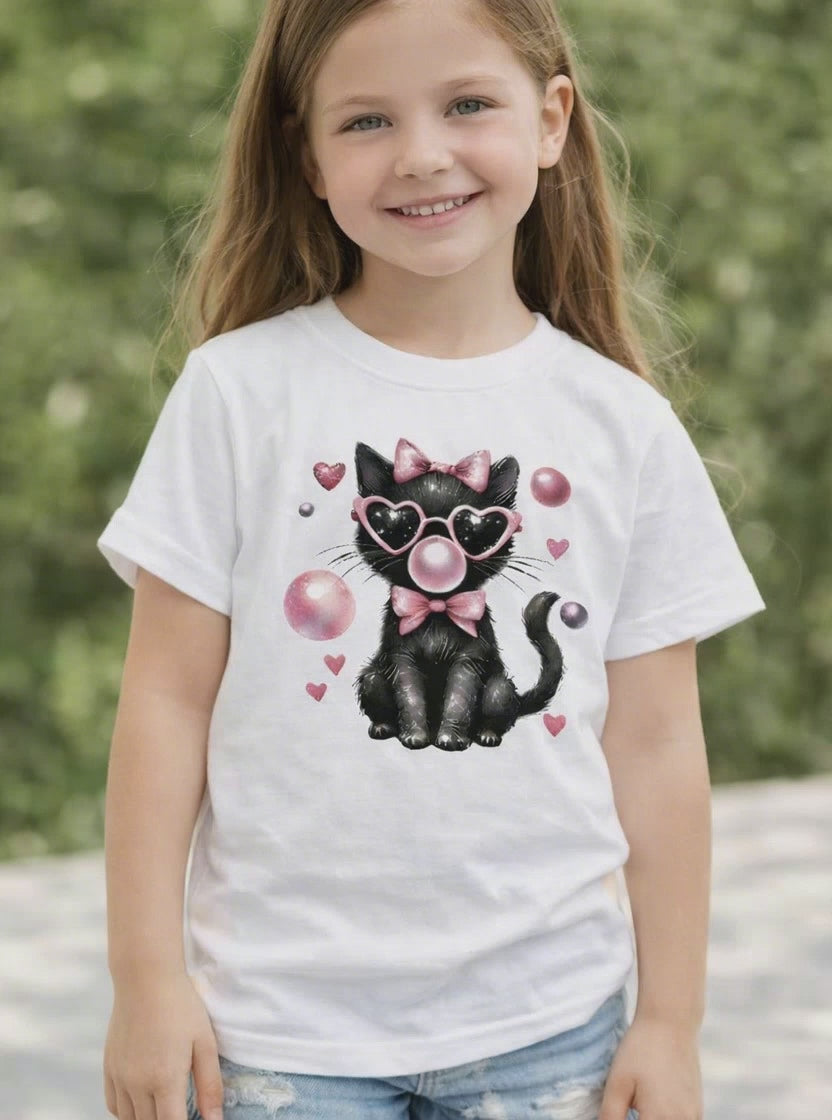 Child wearing a white short sleeve t shirt featuring a black cat Valentine design with pink heart sunglasses, bow, and floating heart accents, shown on a youth model outdoors