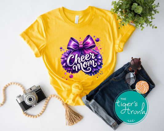 Yellow t-shirt with 'Cheer Mom' design, sunglasses, camera, and denim jacket on a white background.