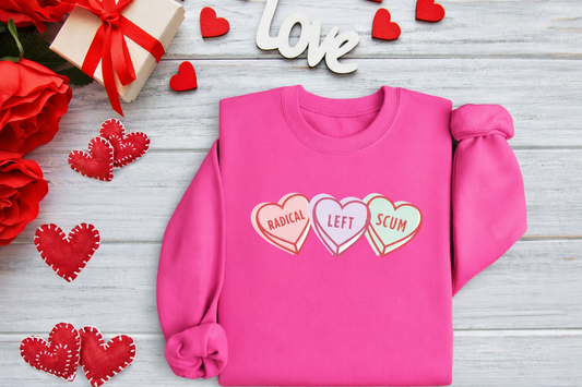 Pink sweatshirt with colorful heart designs on a wooden surface with red flowers and hearts.