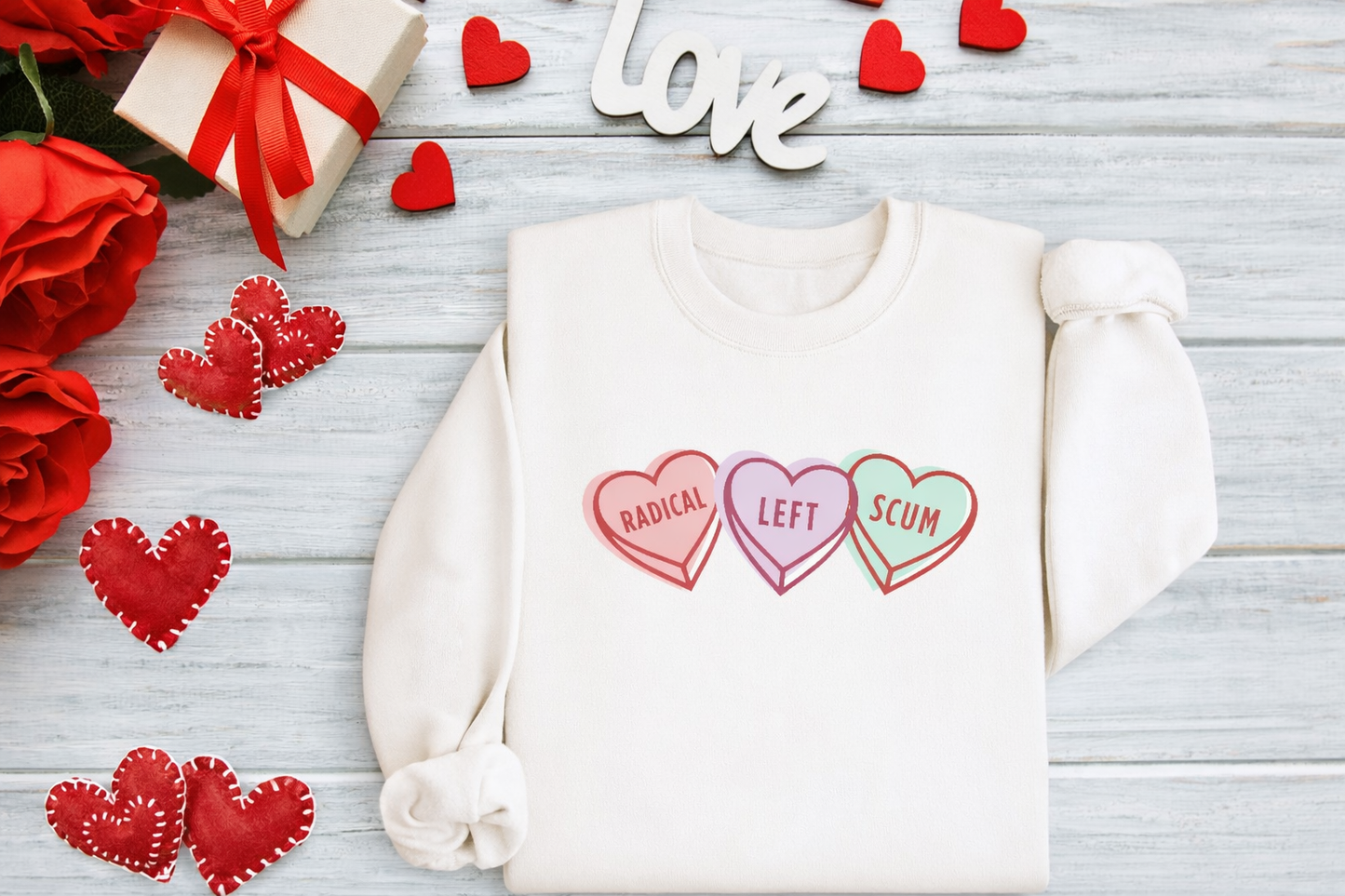 White sweatshirt with colorful heart-shaped text on a wooden surface with red roses and decorative hearts.