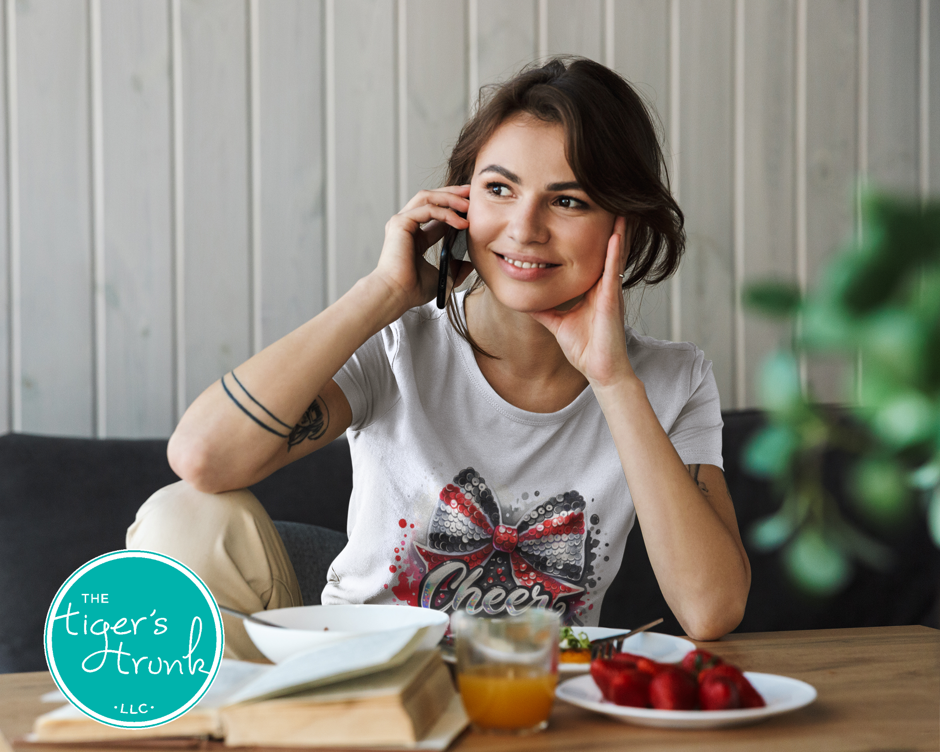 Woman sitting at a table with food and a phone, with 'The Tiger's Trunk' logo in the corner.