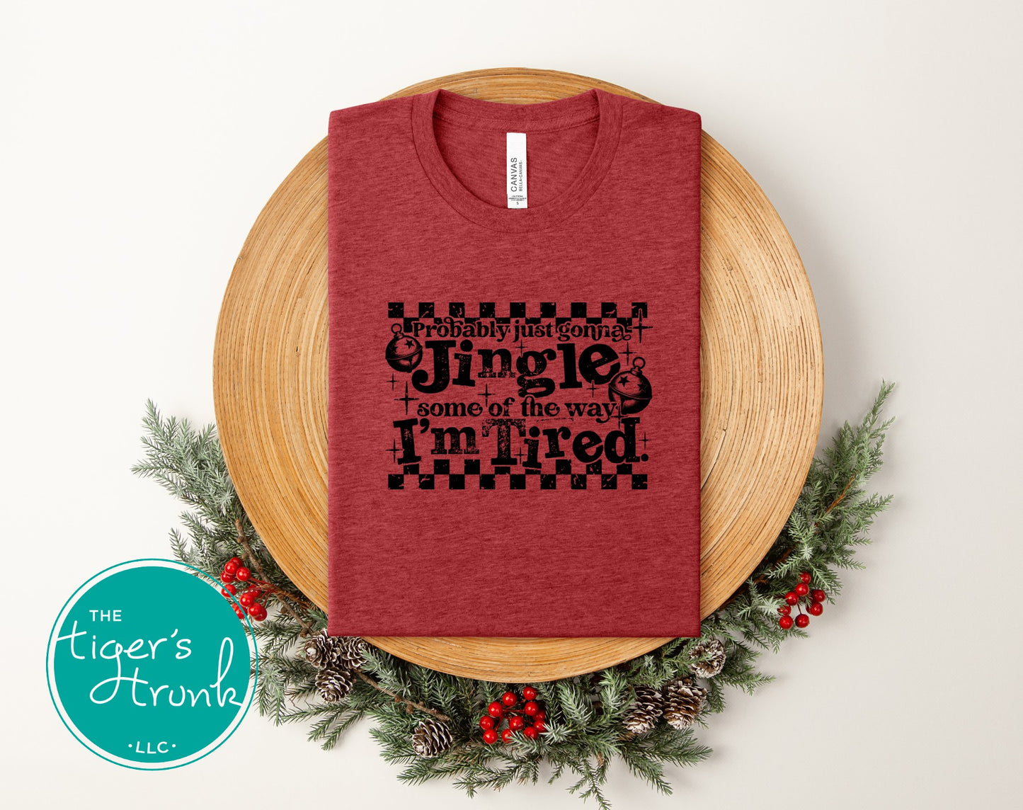 Red t-shirt with Christmas-themed text on a wooden plate with decorative elements, featuring 'The Tiger's Den' logo.