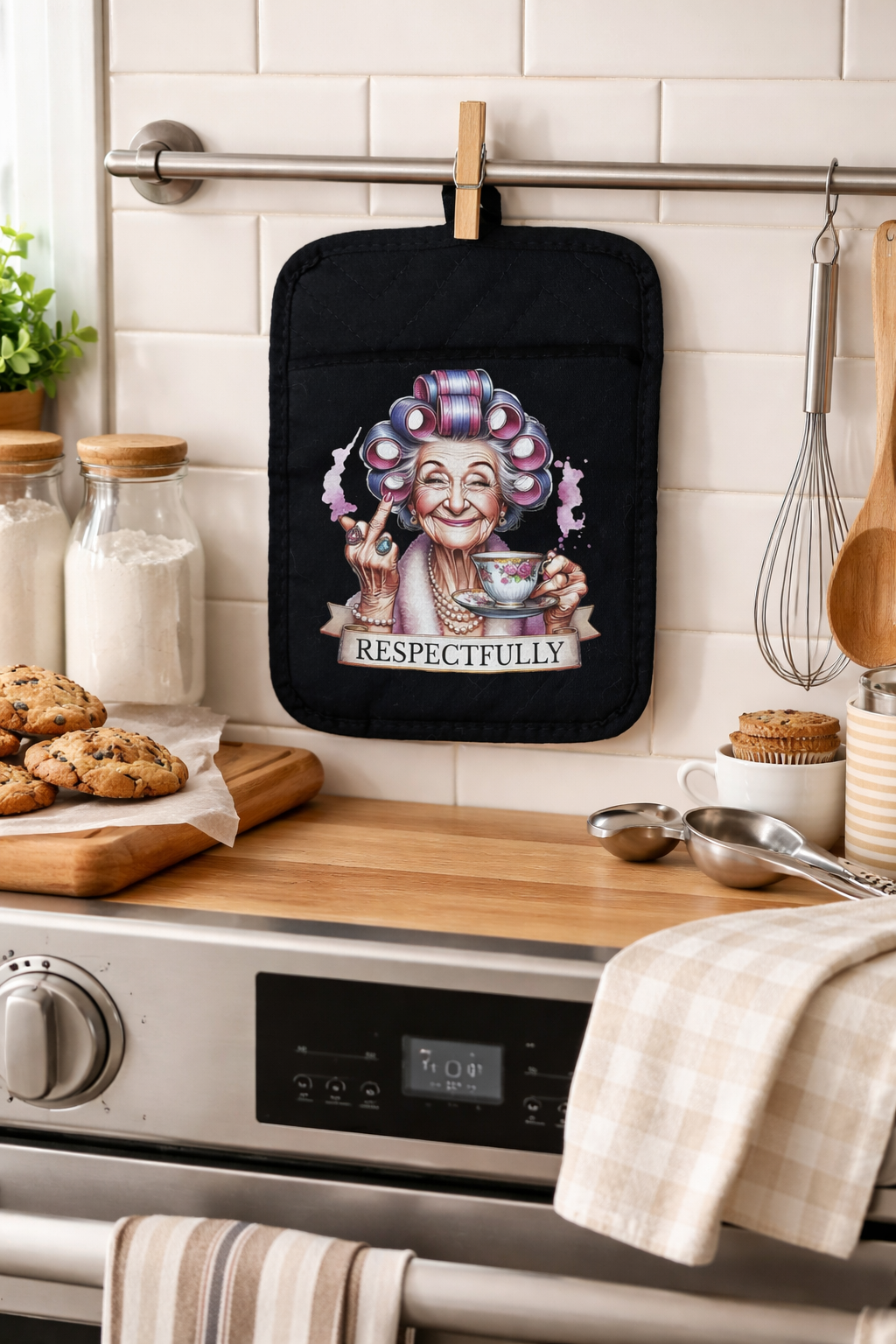 Black pot holder with a colorful design of an elderly woman holding a teacup, hanging on a kitchen wall.