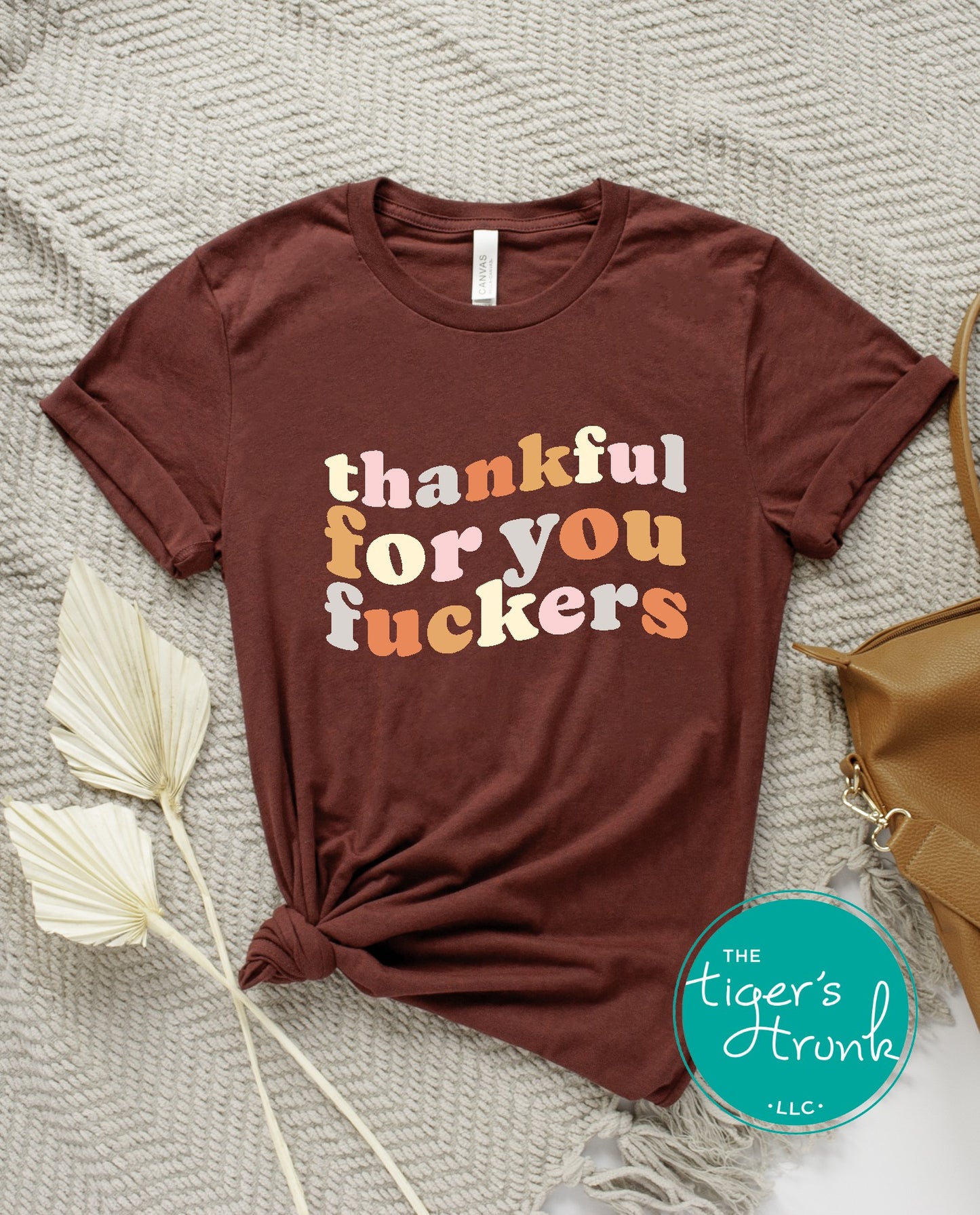 Brown t-shirt with colorful text on a textured surface with a brand logo.