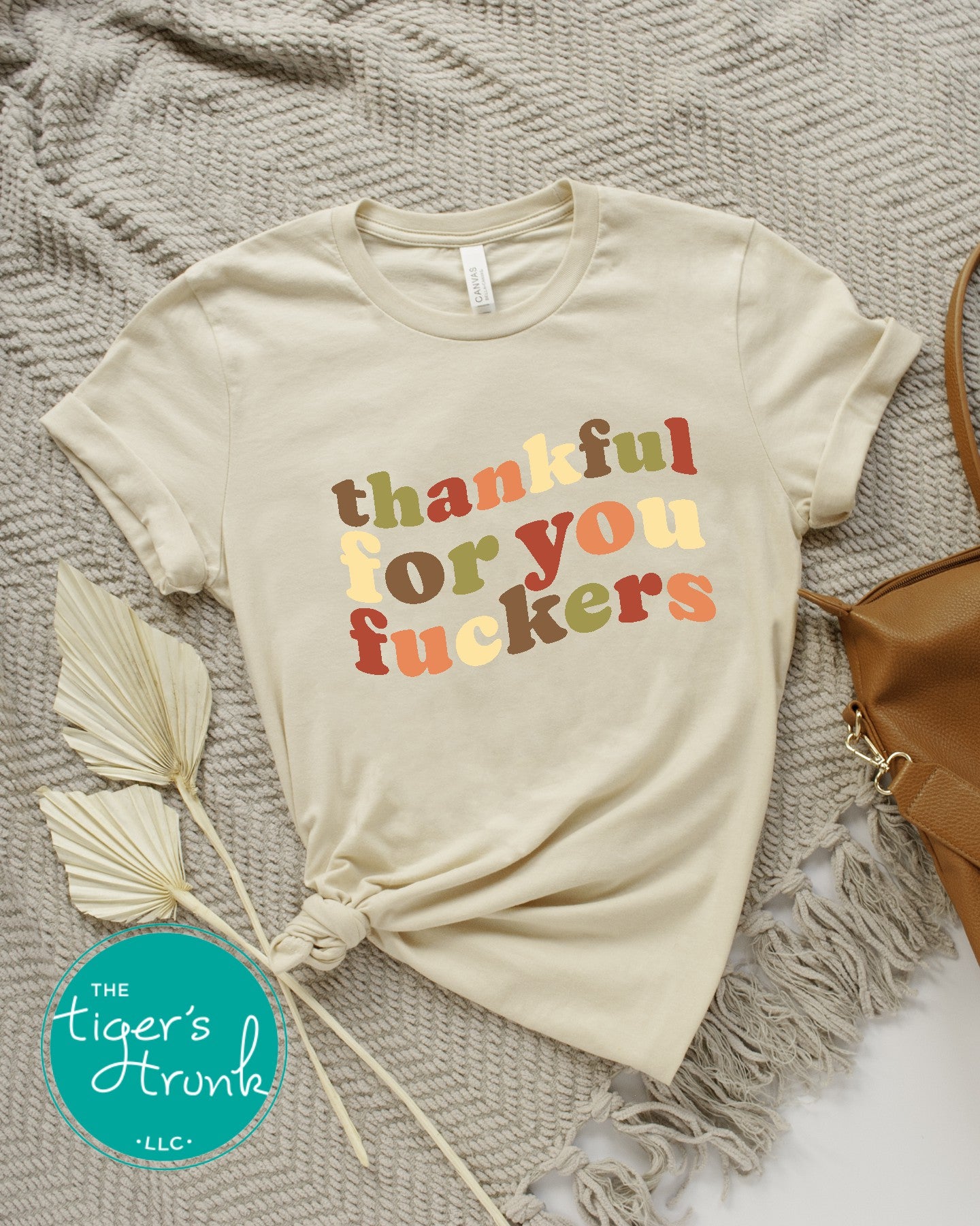 Beige t-shirt with colorful text on a textured surface with a bag and leaves.