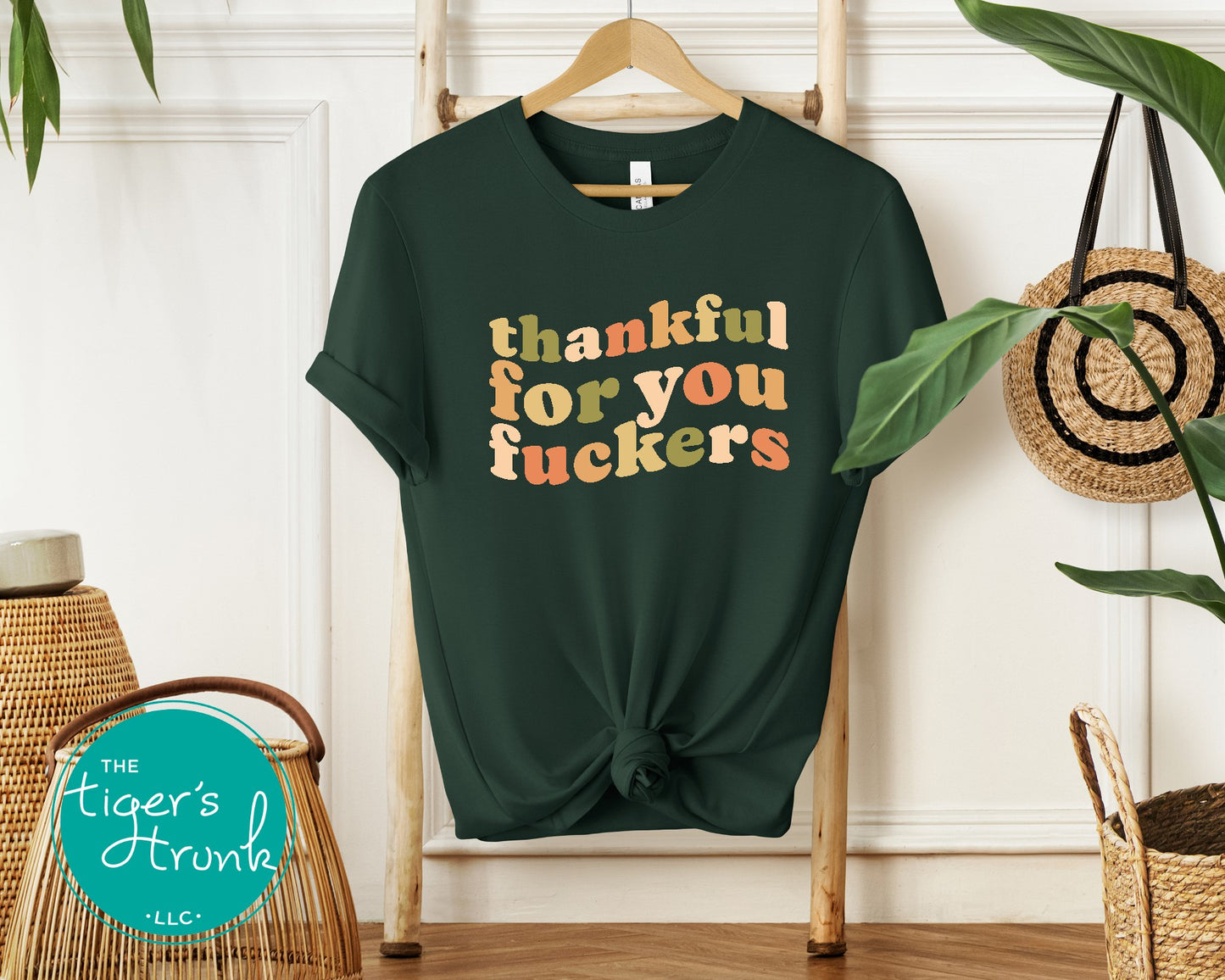Green t-shirt with colorful text on a hanger against a white wall with decorative elements.