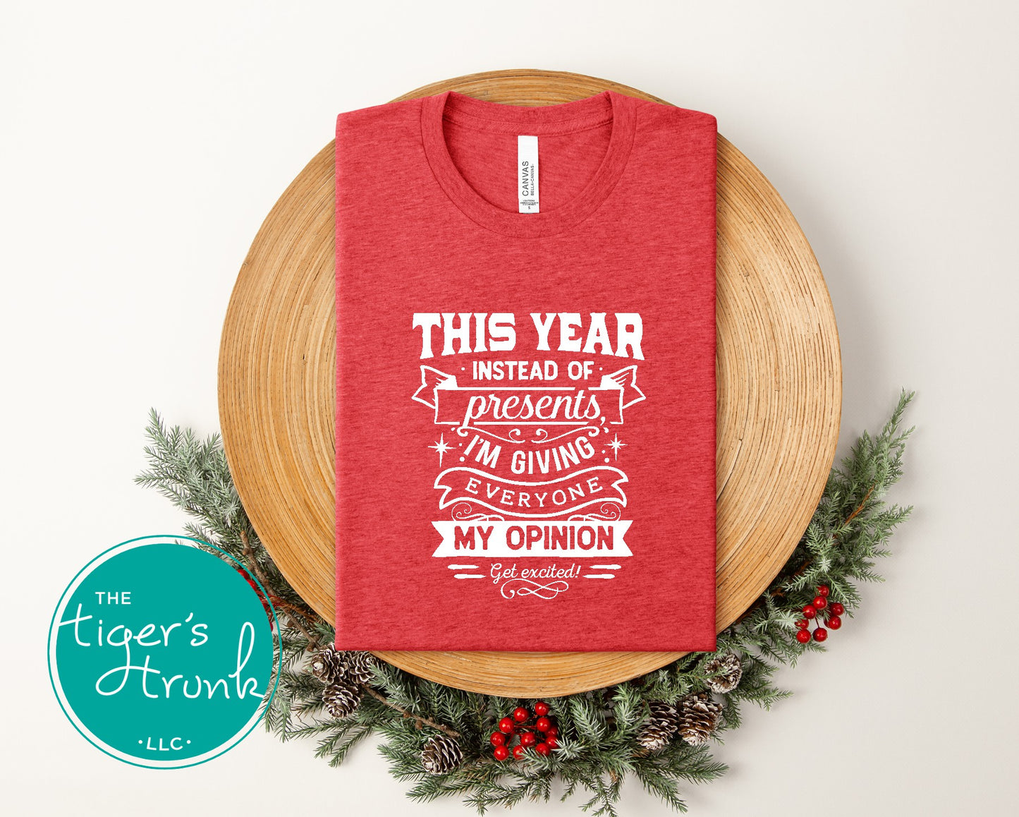 Red t-shirt with humorous text design on a wooden surface with Christmas decorations.