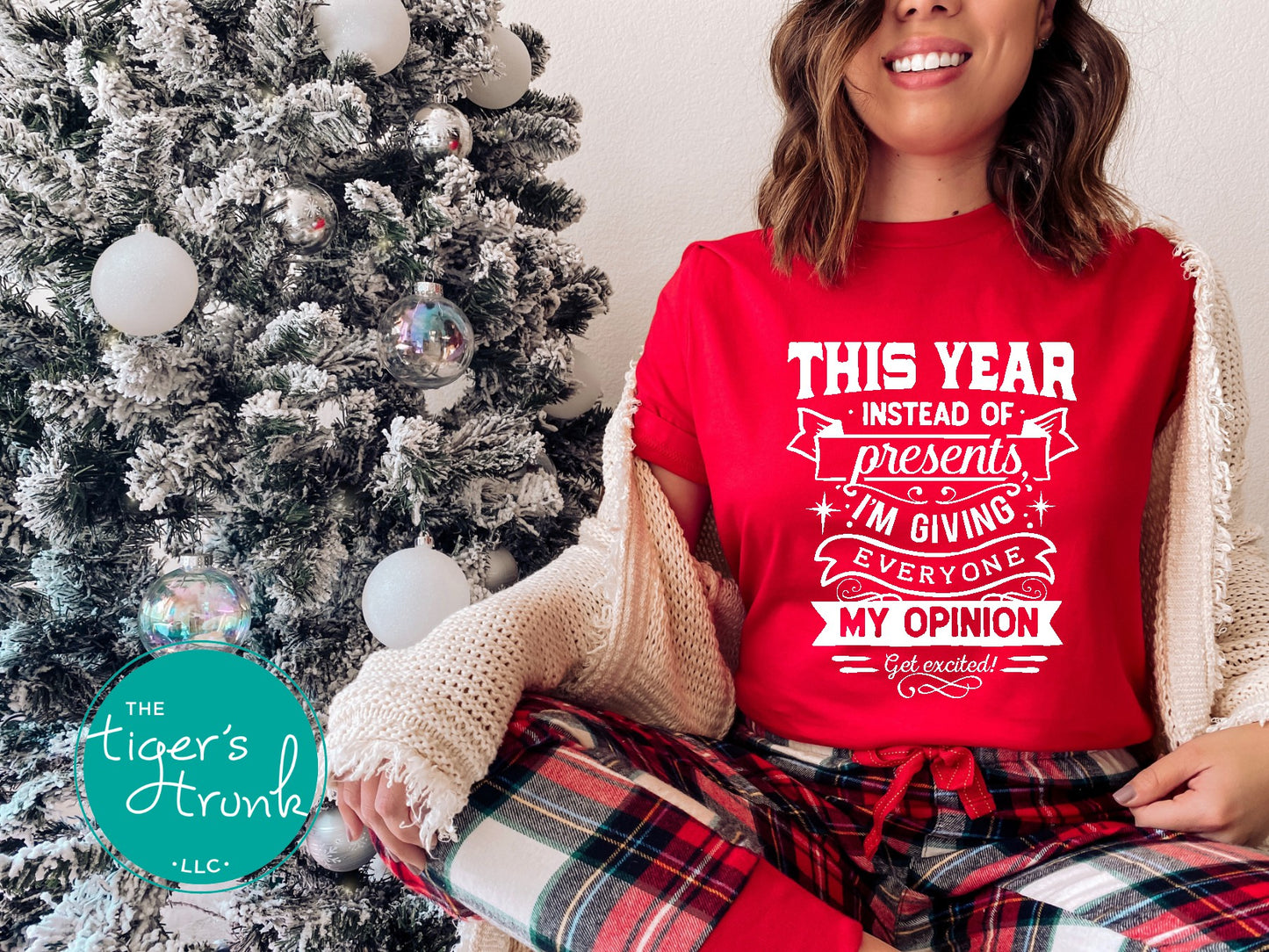 Person wearing a red shirt with humorous text next to a decorated Christmas tree, with 'The Tiger's Trunk' logo.