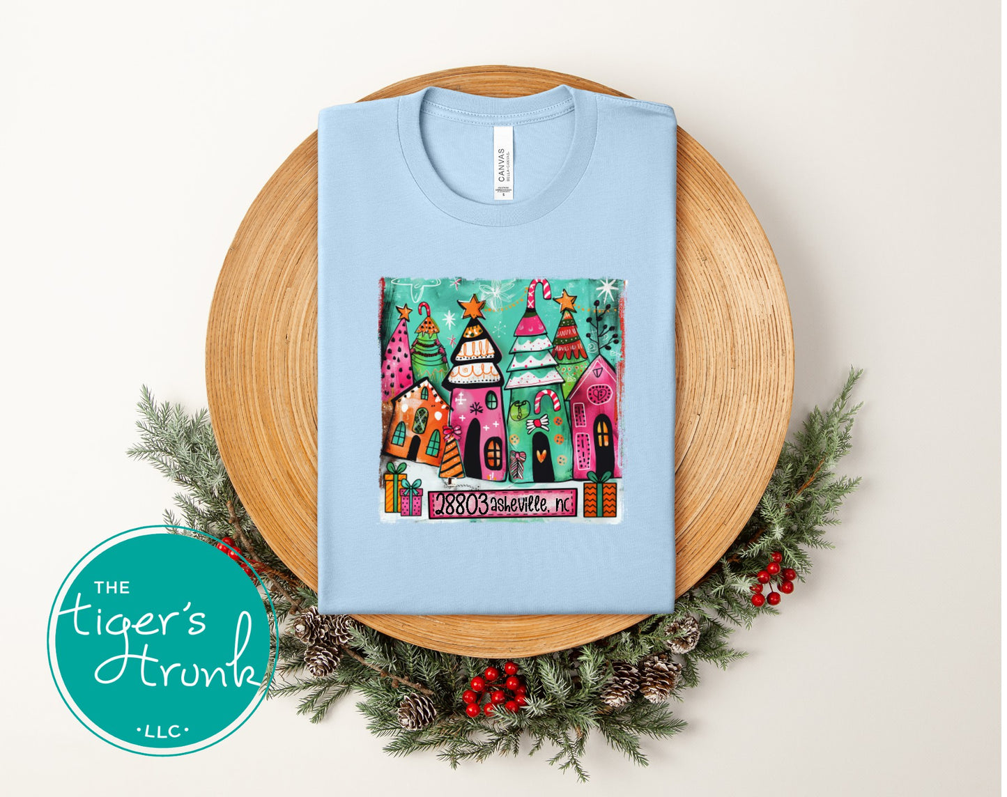 Baby blue Christmas shirt showing colorful painted holiday houses and trees featuring ZIP code 28803 Asheville, NC.