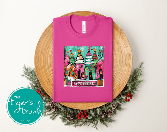 Berry-colored Christmas shirt featuring vibrant painted holiday houses and trees with ZIP code 64157 Kansas City, MO.