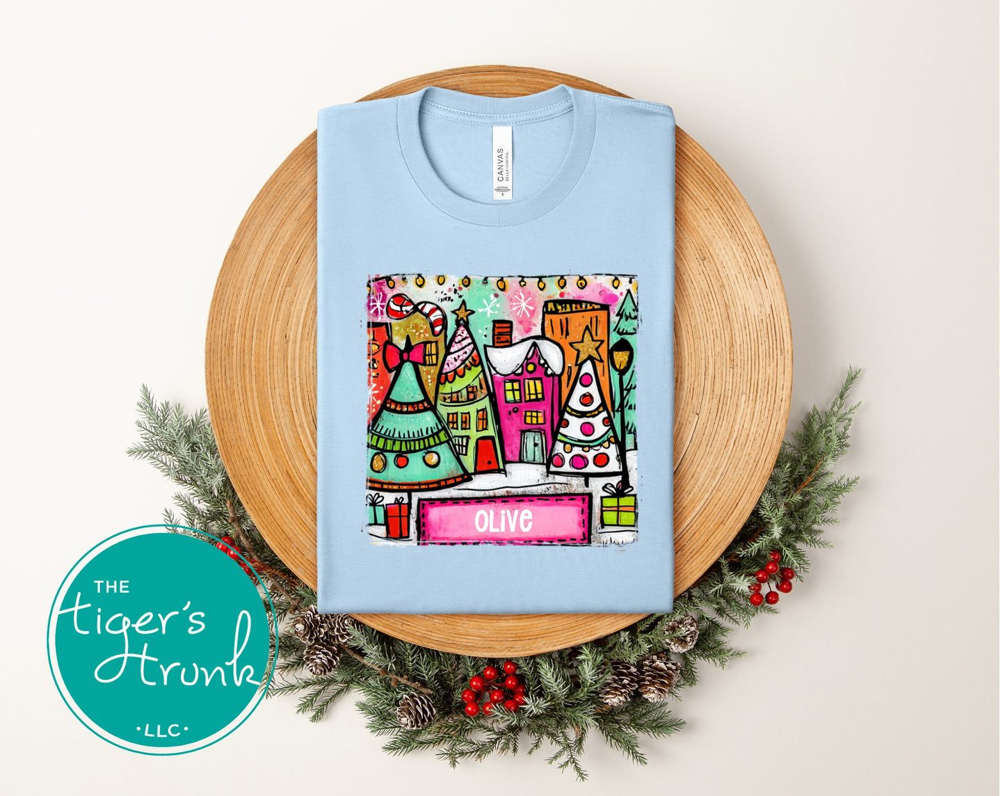 Light blue t-shirt with colorful graphic design on a wooden plate with Christmas decorations.